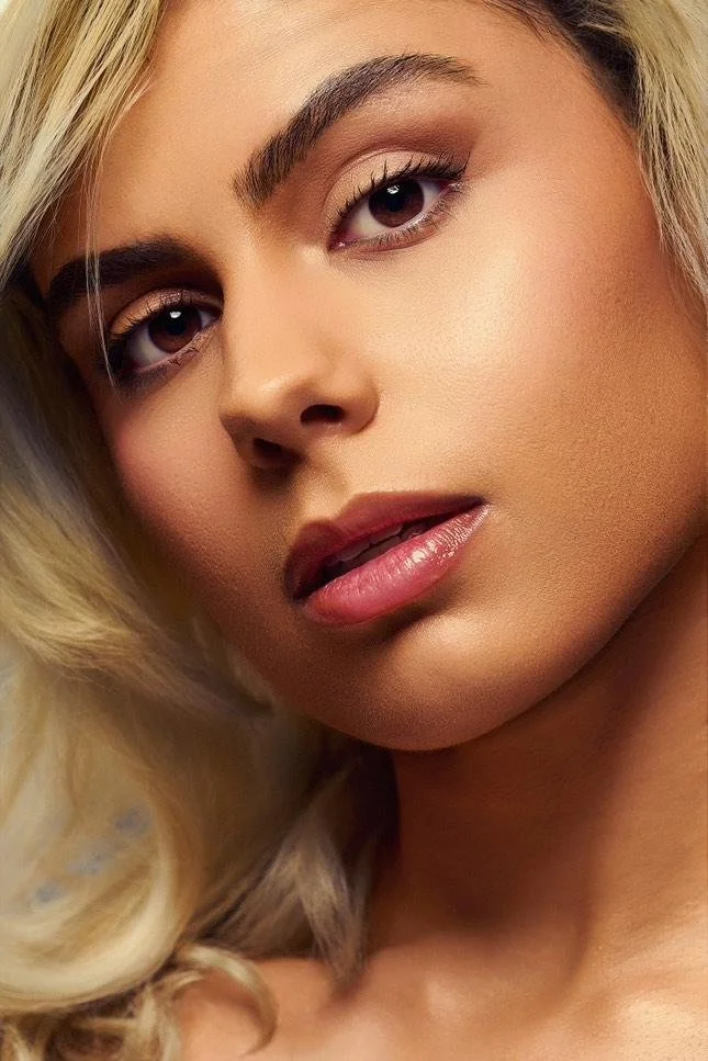 Close-up of a woman with blonde hair, full lips, and well-defined eyebrows, looking directly at the camera.