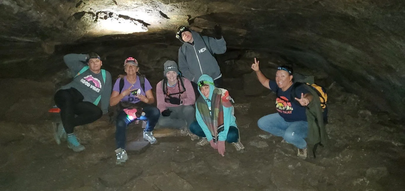 Group of six people inside a cave, wearing helmets and outdoor gear, posing for a photo.