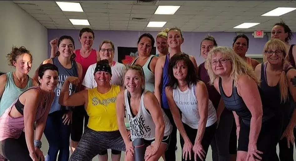 Group of women in workout clothes smiling in a gym studio.