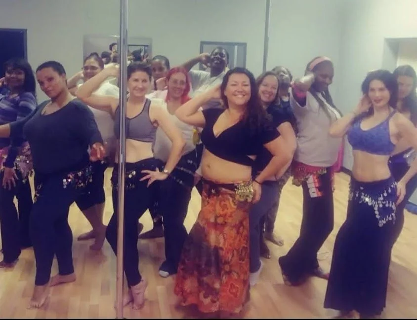 Group of people in a dance studio, dressed in dance costumes, posing at a dance class or performance.
