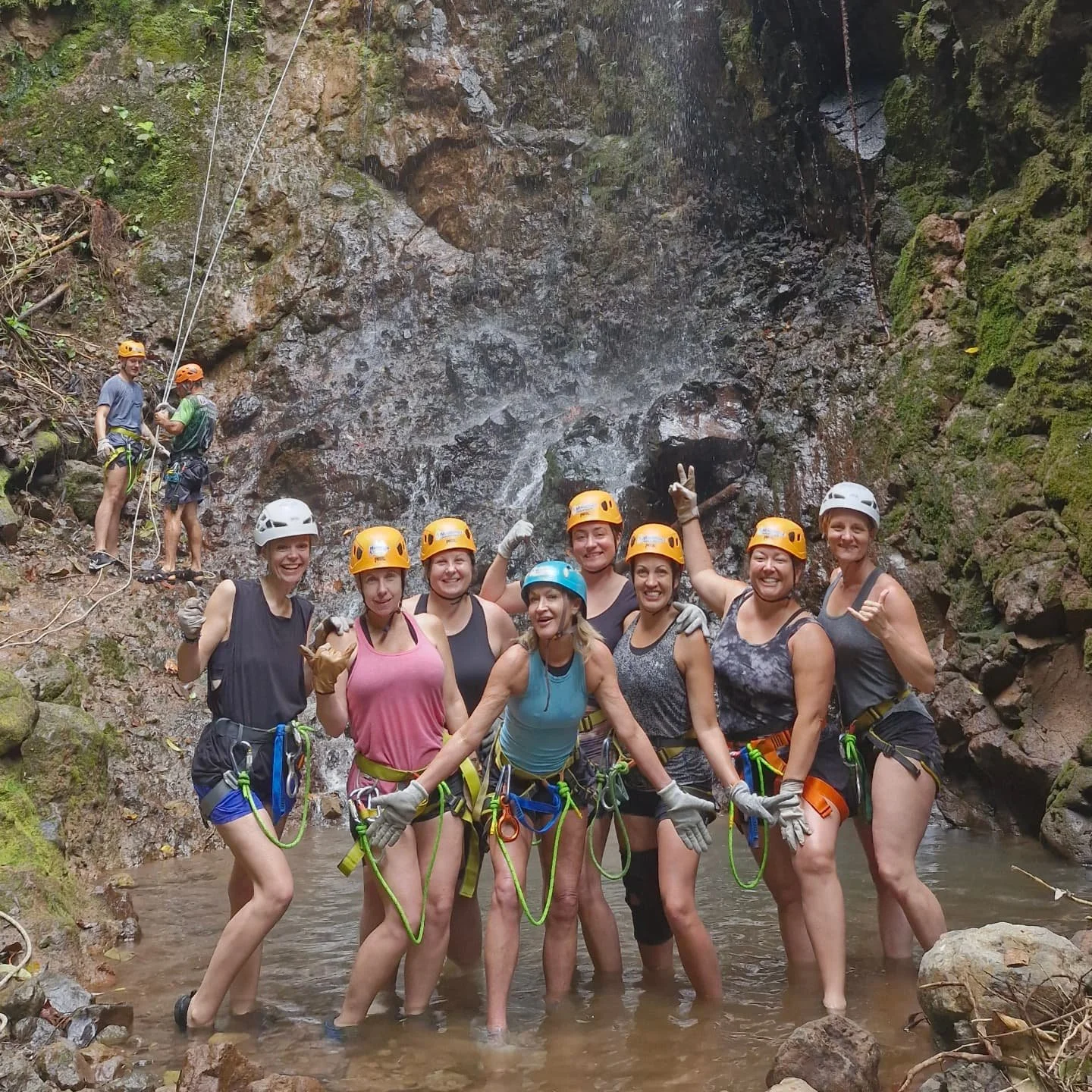 Group of people in climbing gear standing in a river with a waterfall in the background.