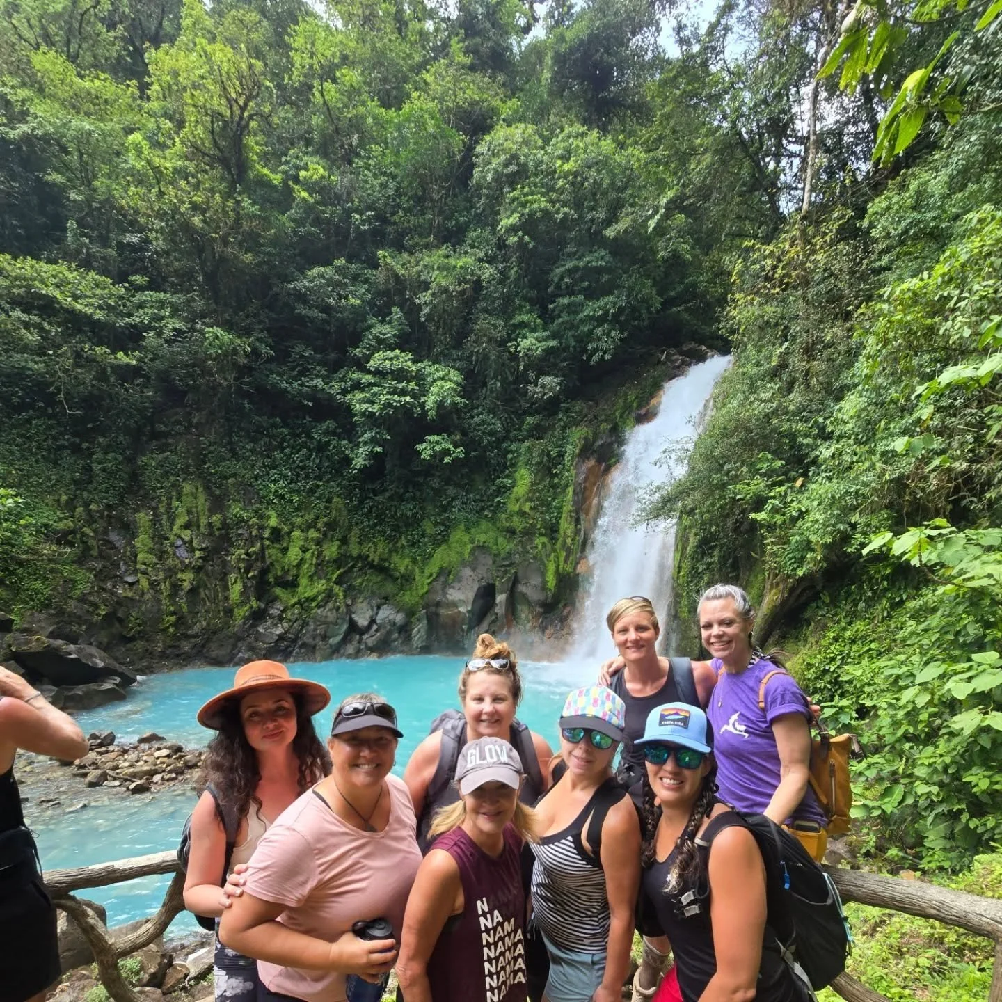 Group of people hiking near a waterfall in a lush green forest.