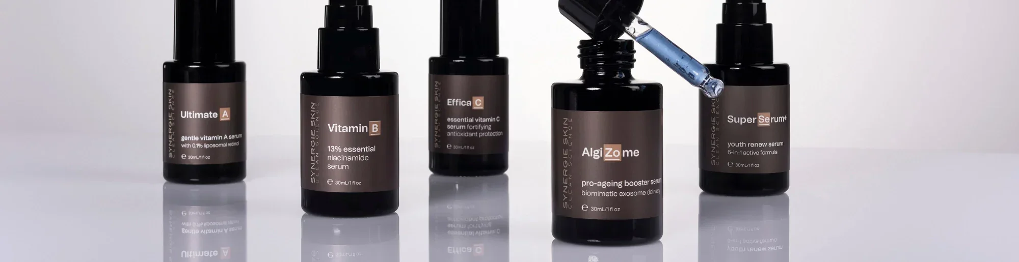 Five dark Synergie Skin bottles with dropper caps and labels displaying different serums, set against a white background.