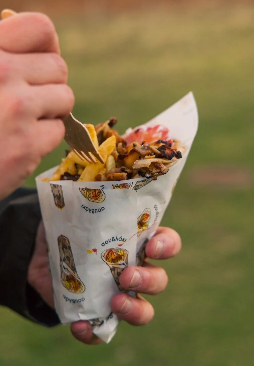 A person holding a wrap with Greek fries, grilled chicken gyros, and salad outdoors.