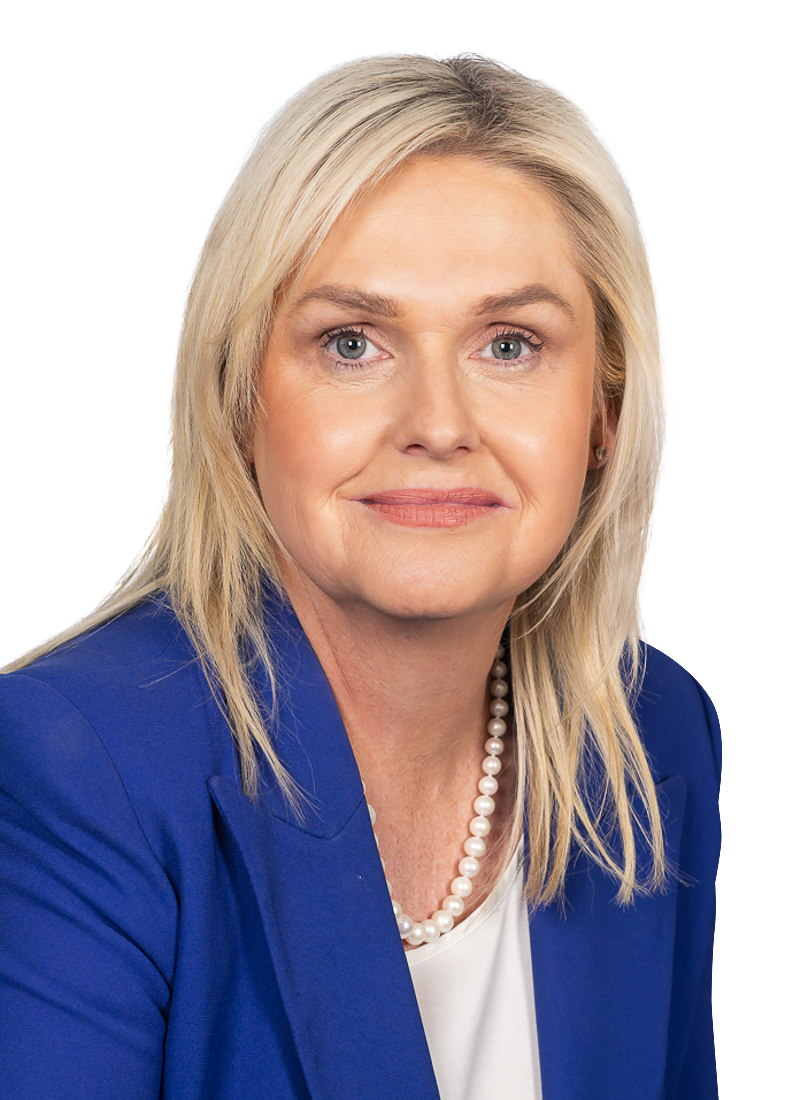 A woman with blonde hair, light skin, wearing a blue blazer, white top, pearl necklace, and earrings, looking at the camera with a neutral expression.