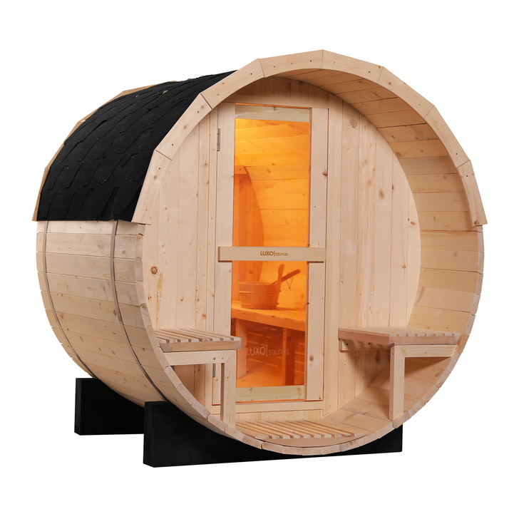 A wooden outdoor sauna in a snowy forest with snow-covered hot tub and bench, surrounded by snow-laden pine trees and a fence.