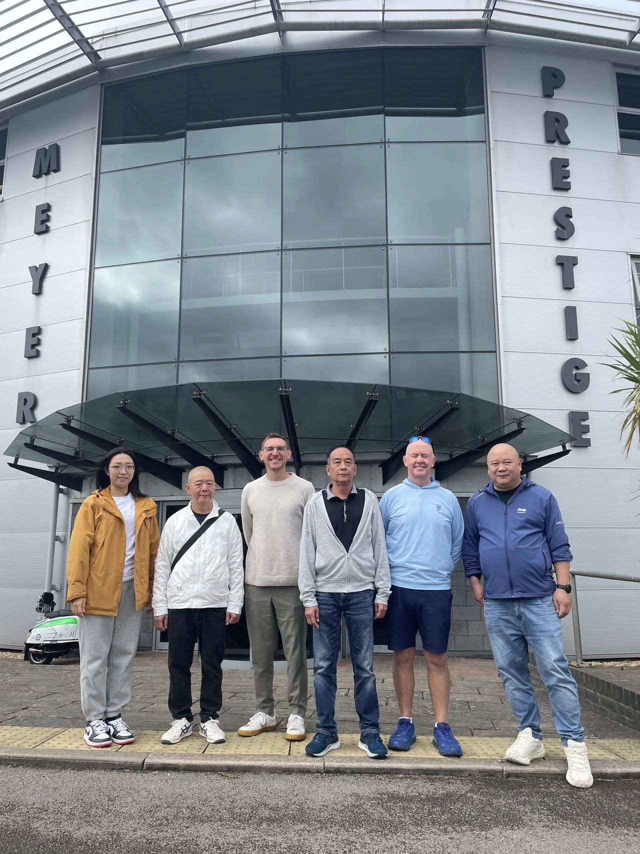 Group of seven people standing in front of a building with the sign "Meyere Prestige" and large glass windows.