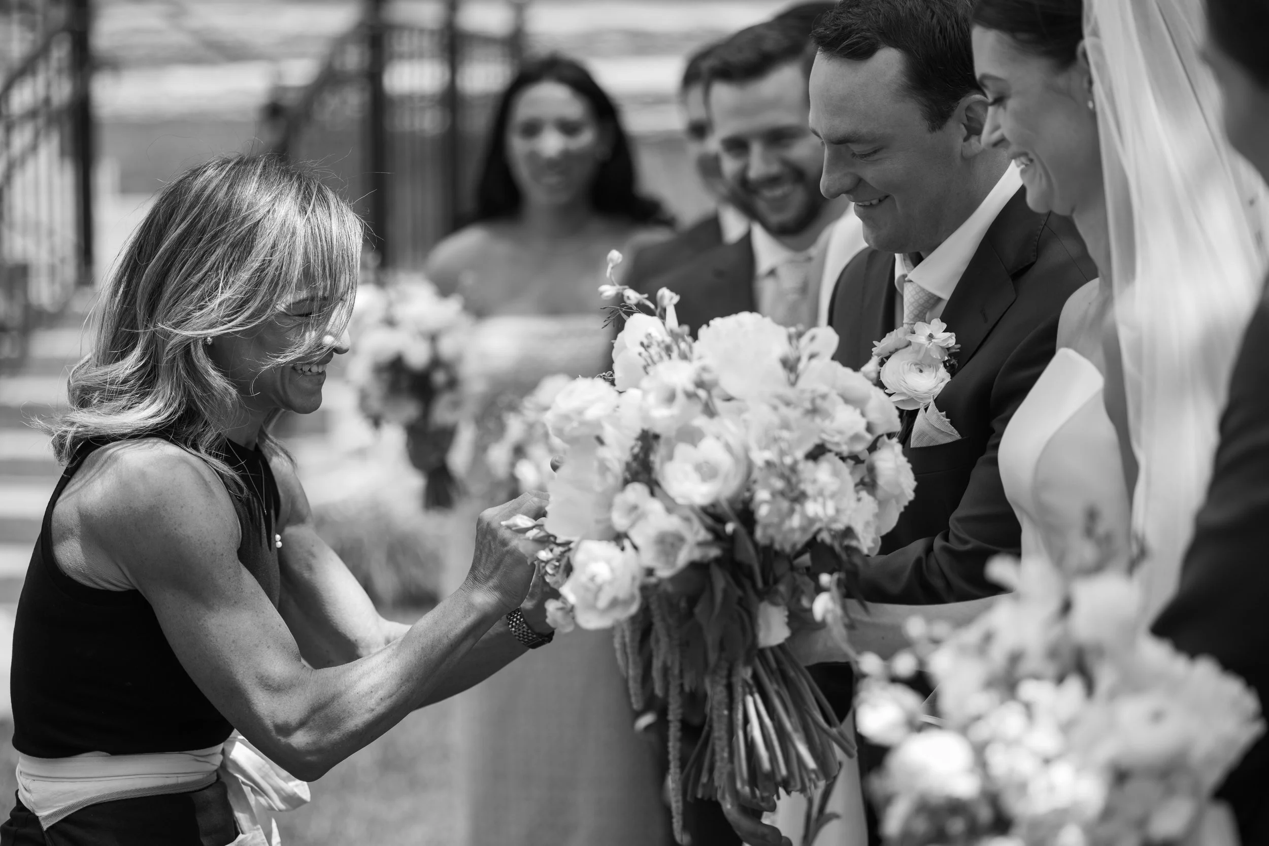 Julia LaCroix adjusting wedding flowers beside a smiling bride and groom.