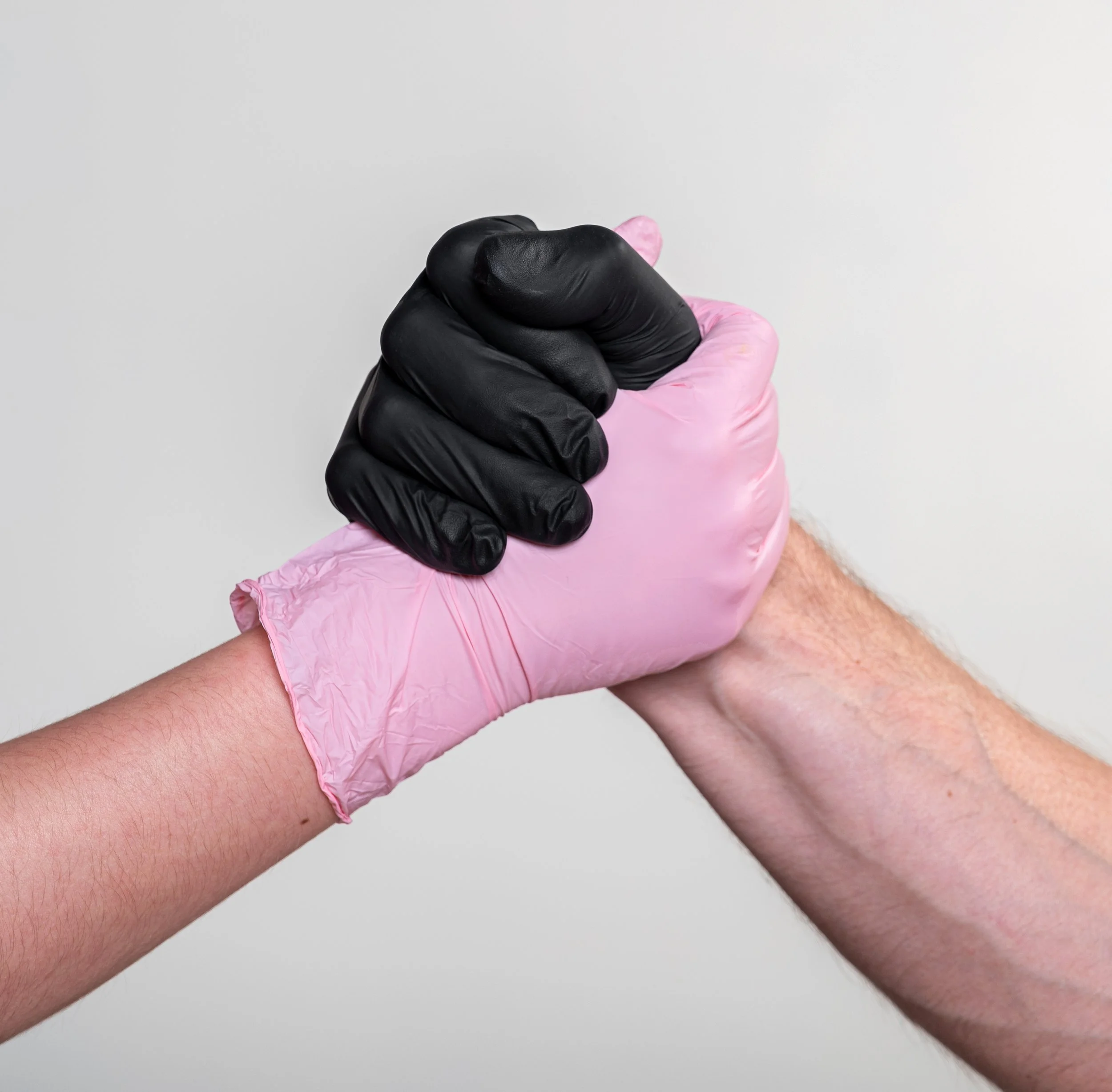 Handshake between two people wearing nitrile gloves - one black and one pink - against a light background