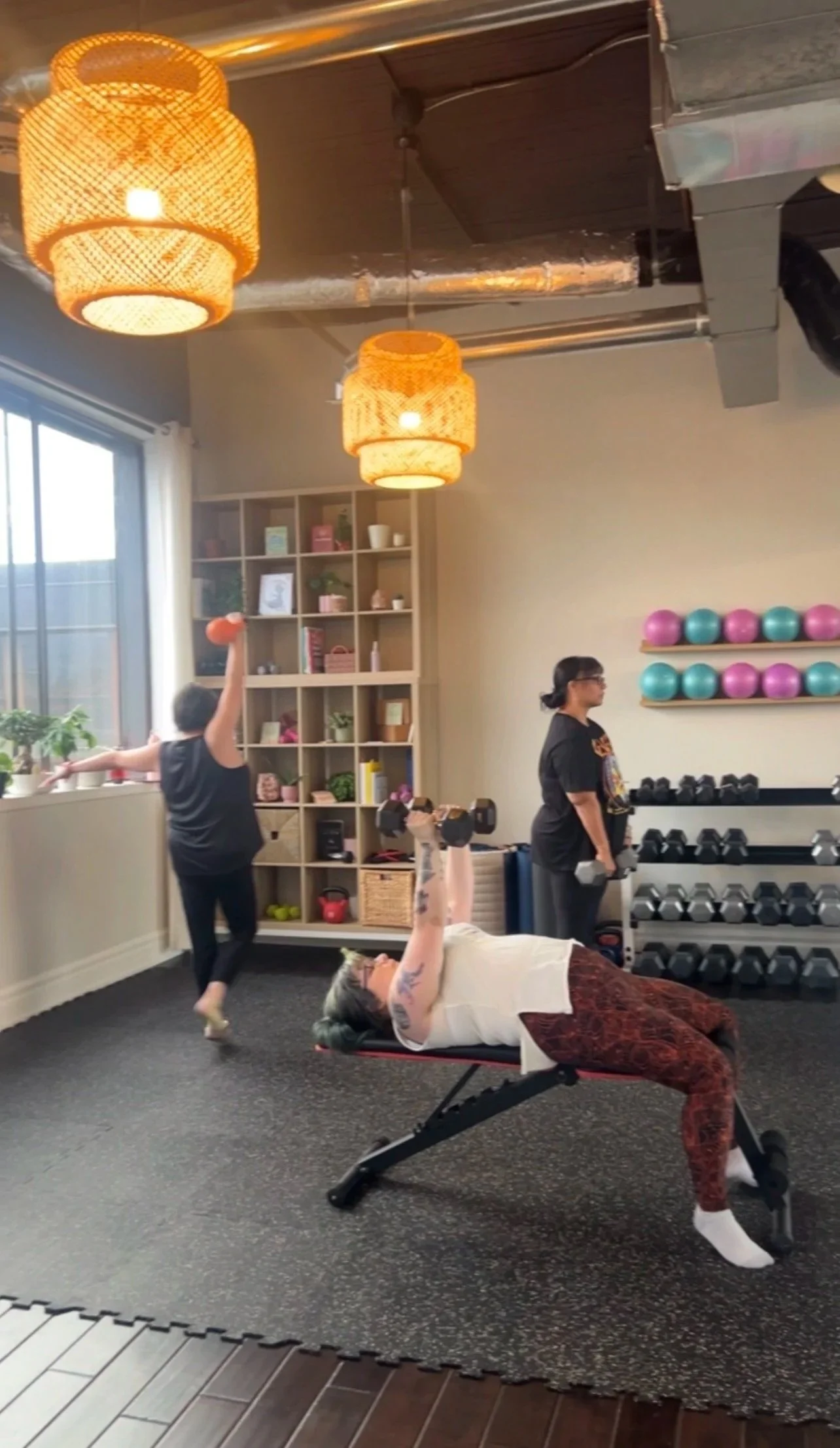 Client in athletic wear doing a bent-over kettlebell exercise in a gym with another person using a bench in the background.