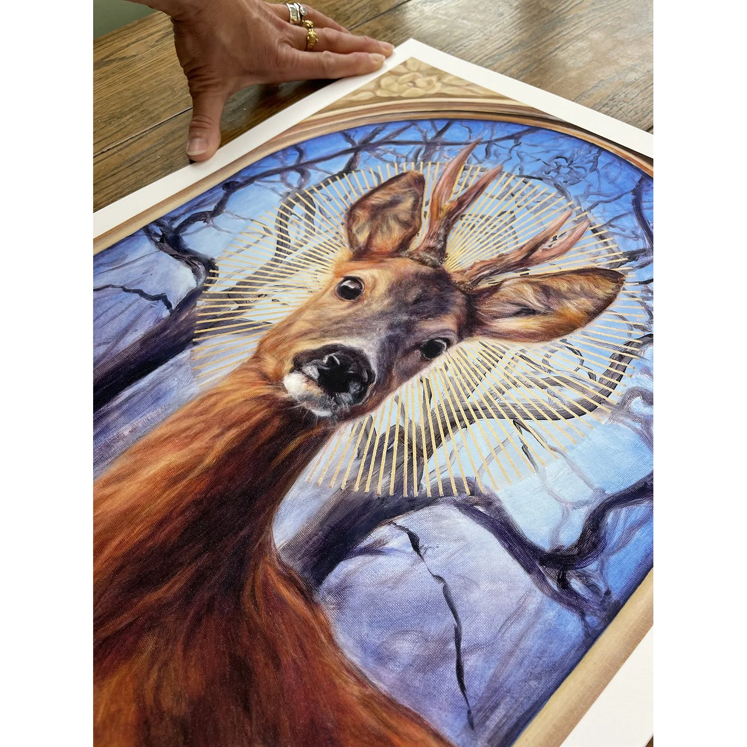 An art print of a handsome roe deer buck with a halo against a background of winter trees. Available to purchase. By imaginative realism artist Karina Tarin.
