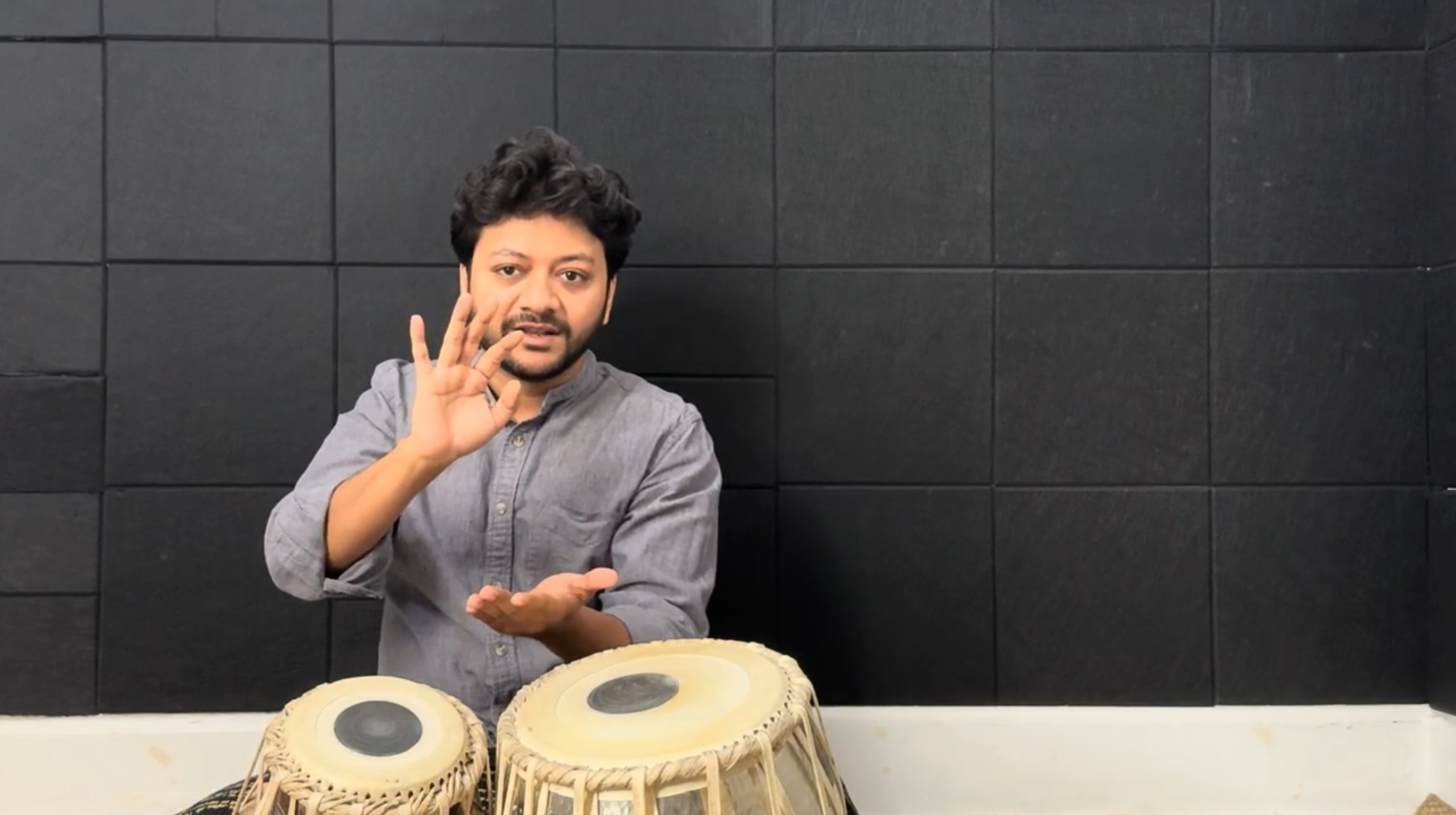 Mir Keherwa Tal demonstrating tabla playing with a black tiled wall in the background.