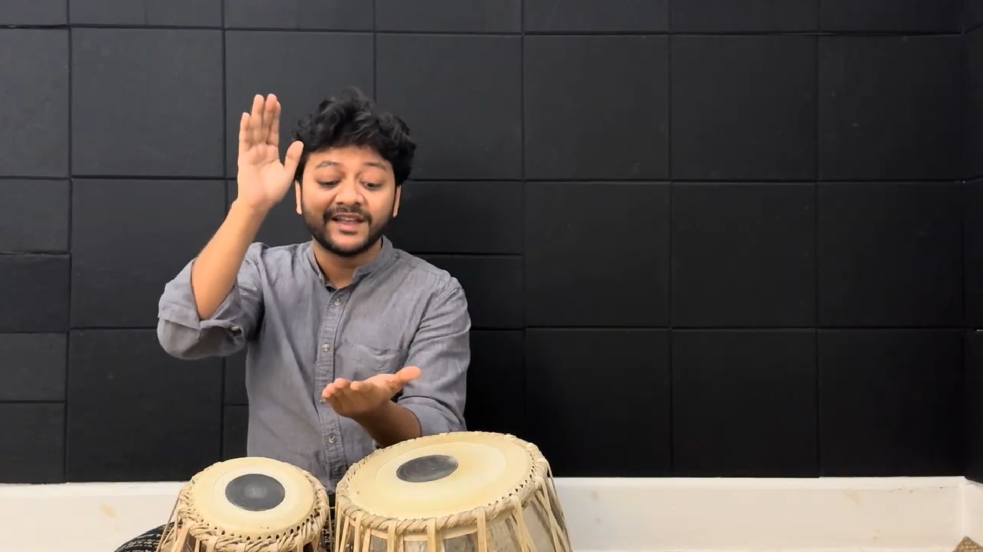 Mir Naqibul Islam demonstrating tabla playing in front of a black soundproof wall.