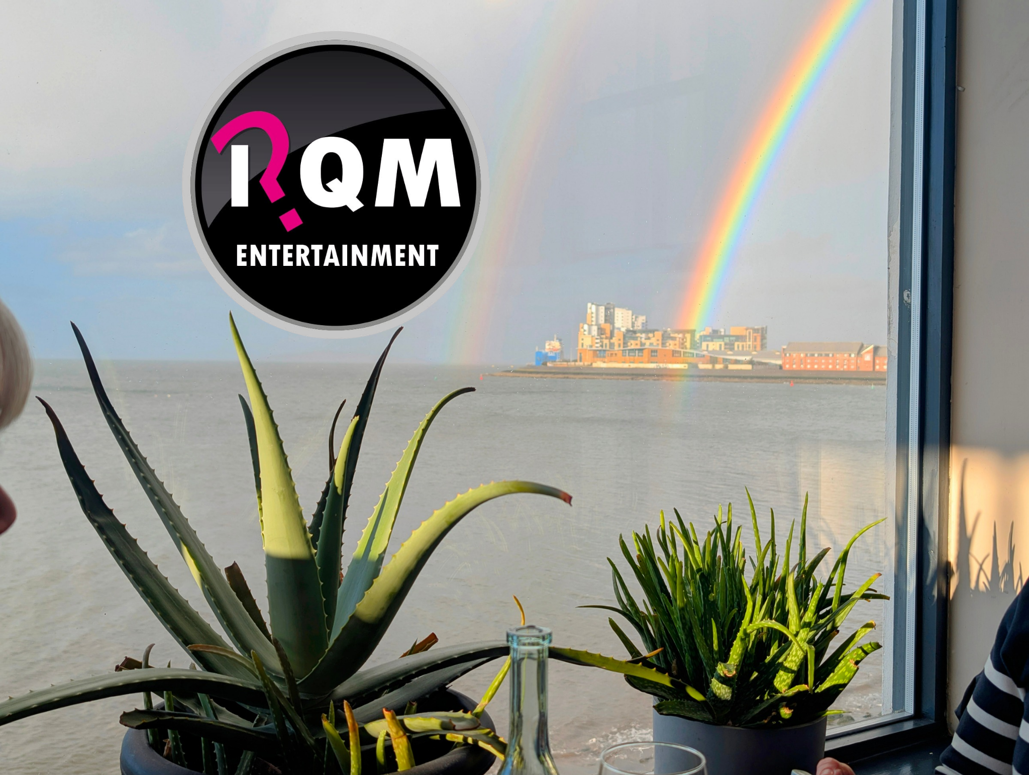 View of colorful rainbow in sky seen through a window, with potted plants on a table in the foreground.
