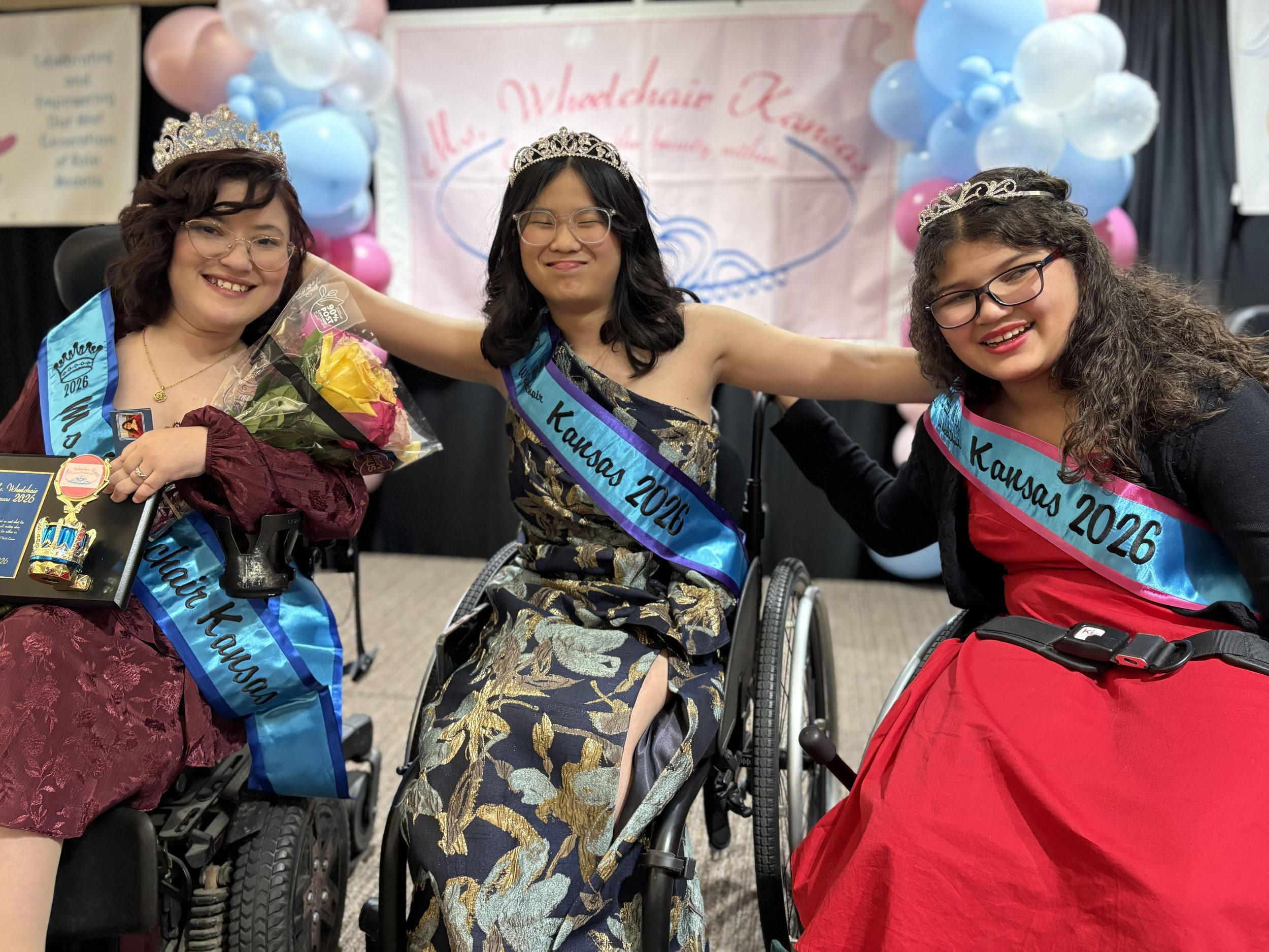 All three new titleholders smile and take a photo together on stage with their arms around each other.