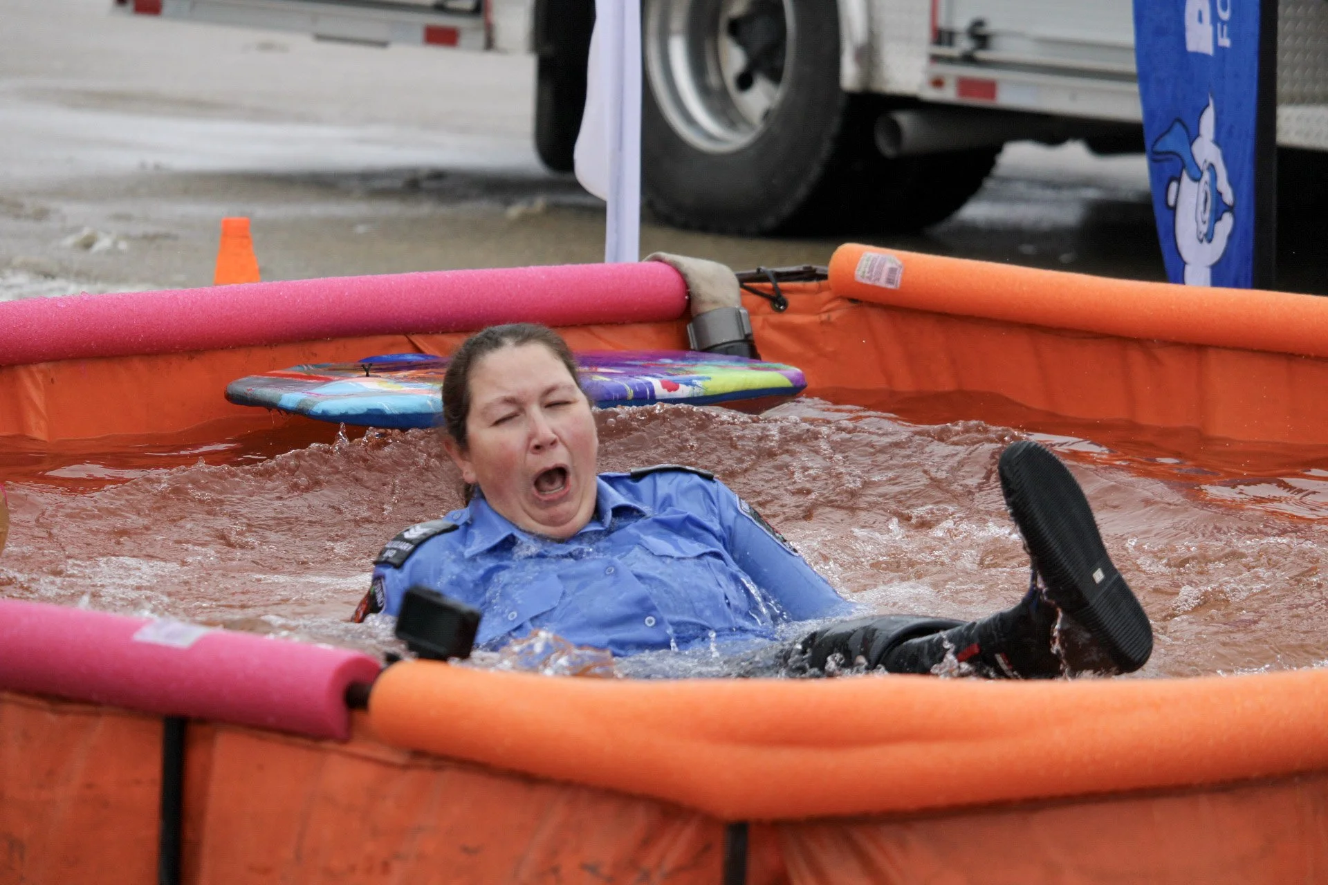 A woman in a police uniform falling into a large orange water tank, with a distressed expression on her face.