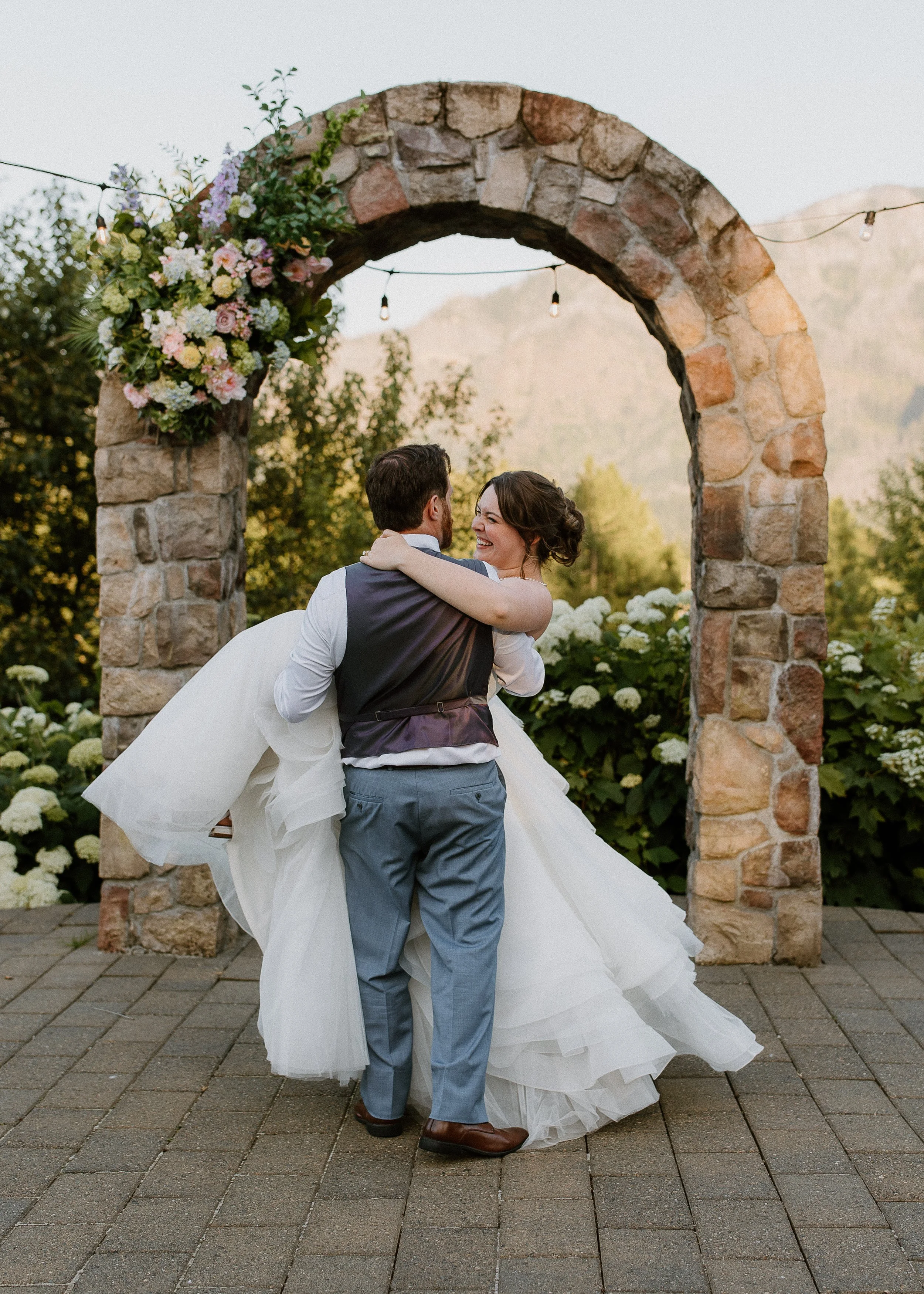 Bride and groom beneath silk wedding flower swag on stone arch