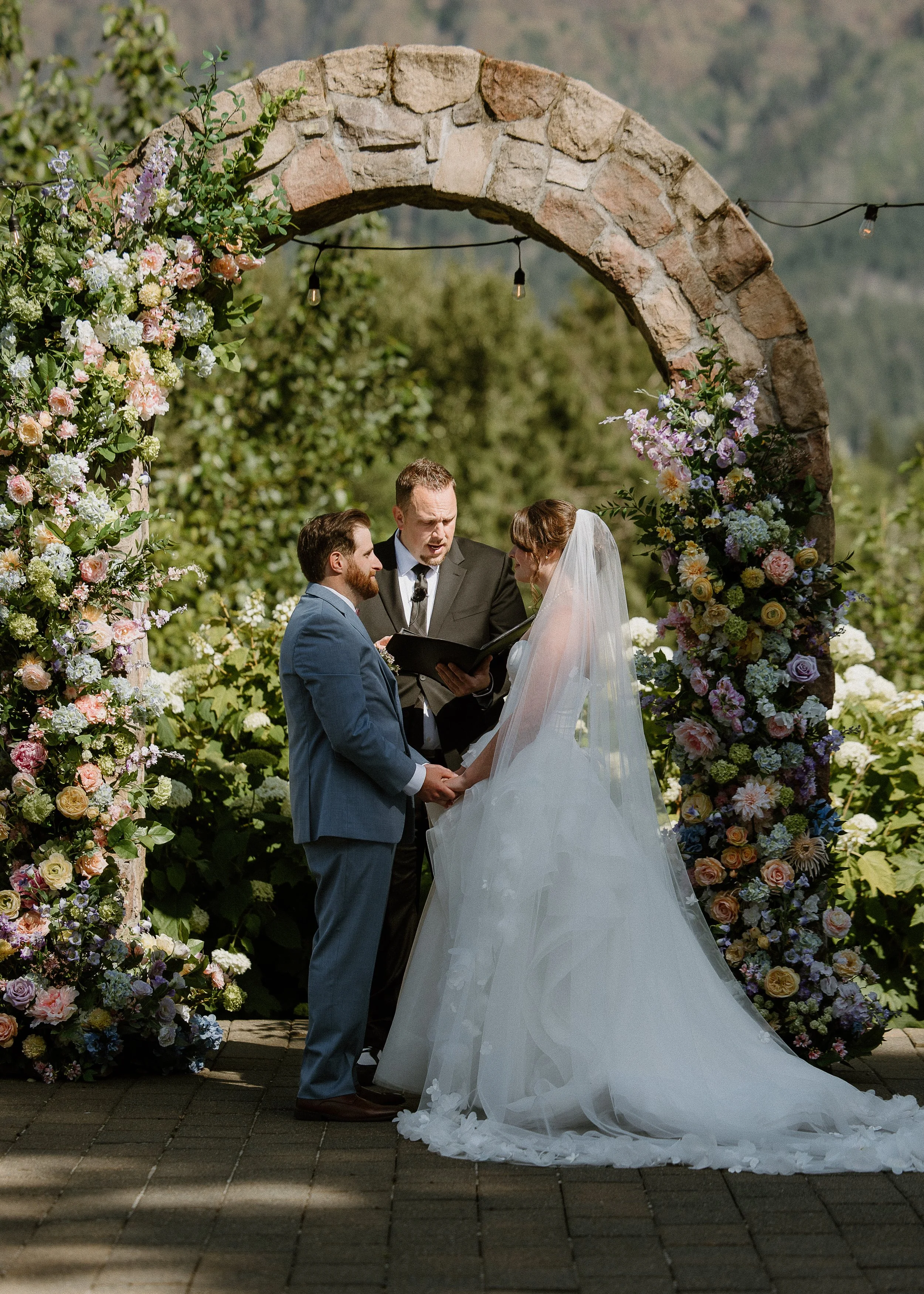 Bride and groom exchanging vows beneath a silk floral wedding arch
