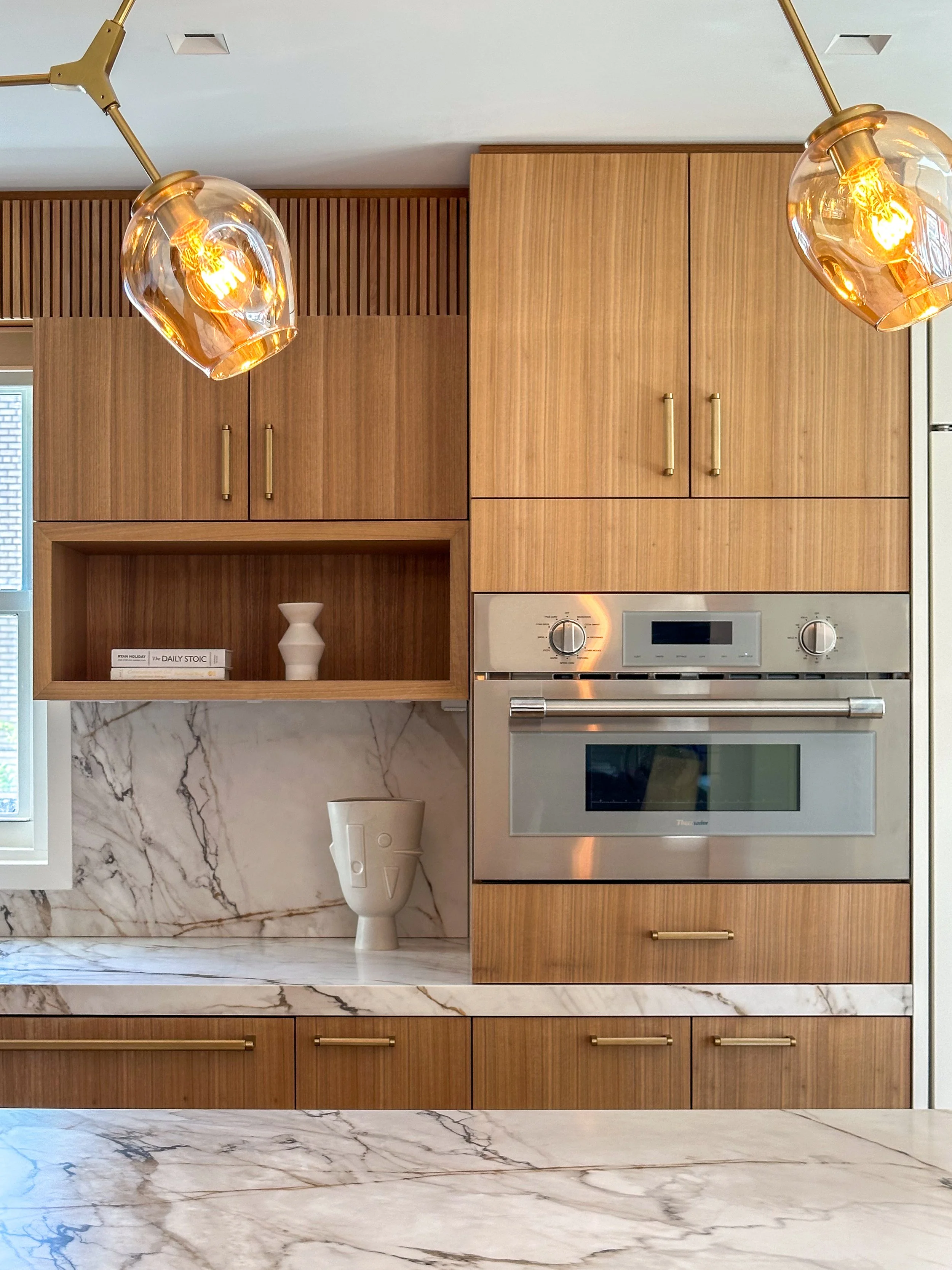 Modern kitchen with wood cabinets, marble countertops, stainless steel oven, decorative vases, and pendant lighting.