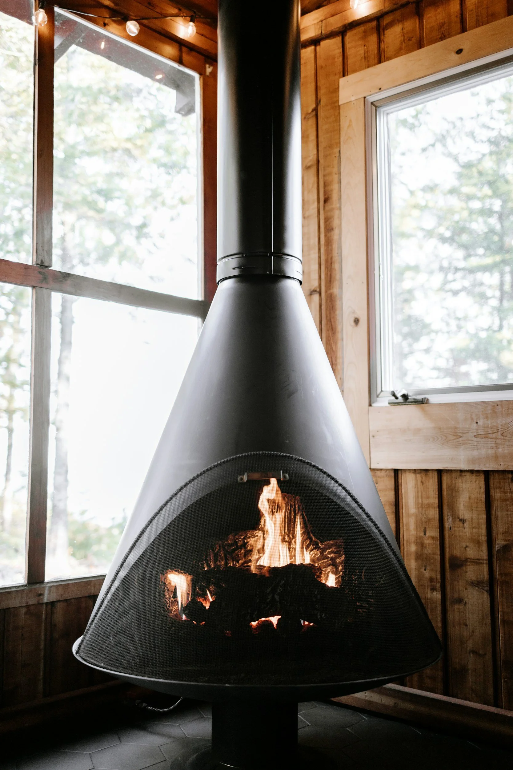 A wood stove burning beside windows looking out on snowy trees