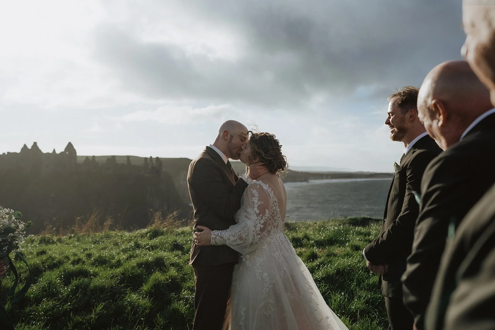 A bride and groom share their first kiss at their elopement at Dunluce Castle in Northern Ireland. There are cliffs and the sea in the background.