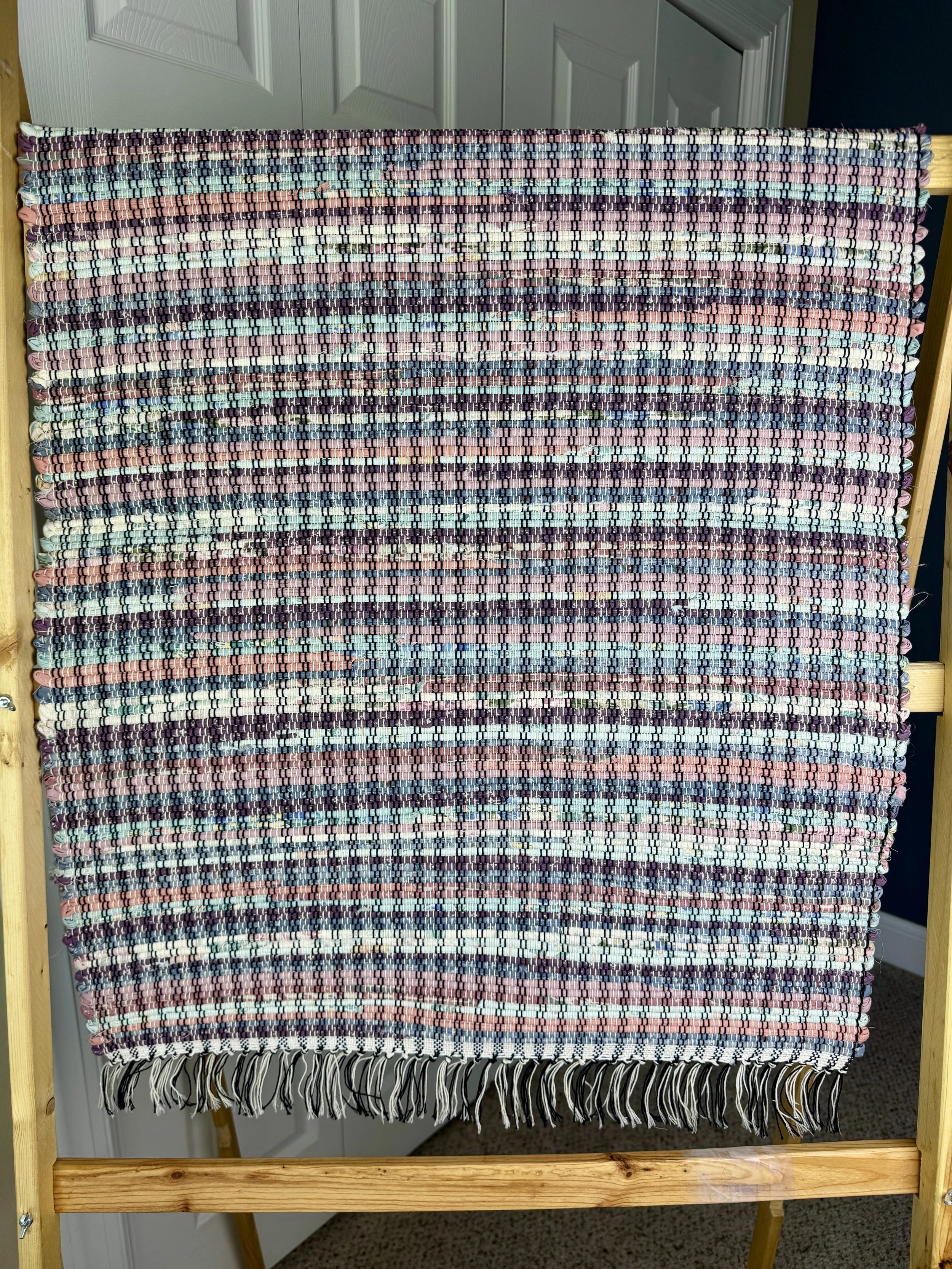 Hanging handmade recycled cotton rag rug showing pattern and fringe