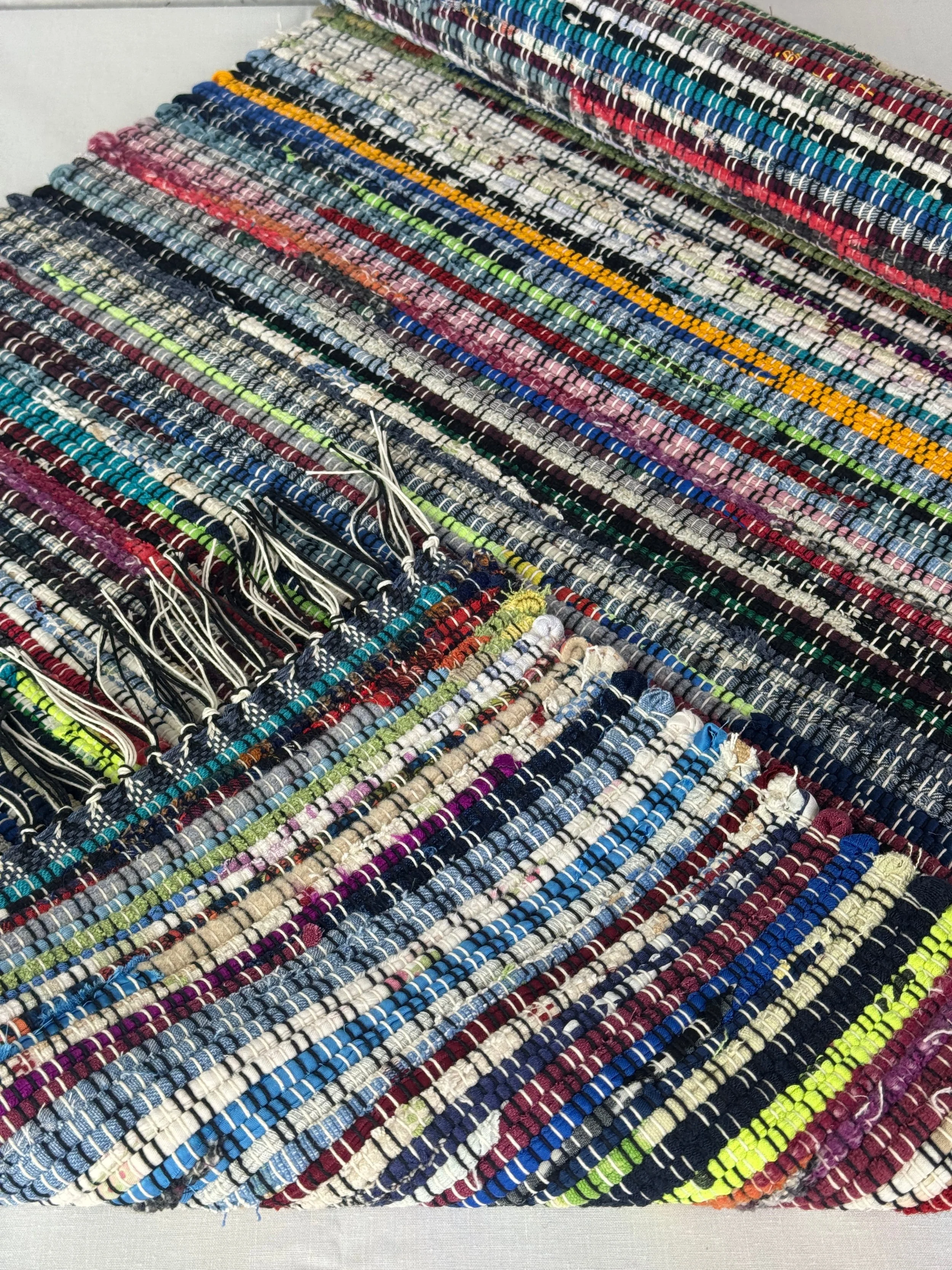 Folded handwoven colorful rag rug from recycled cotton and cotton blends showing reverse side and fringe