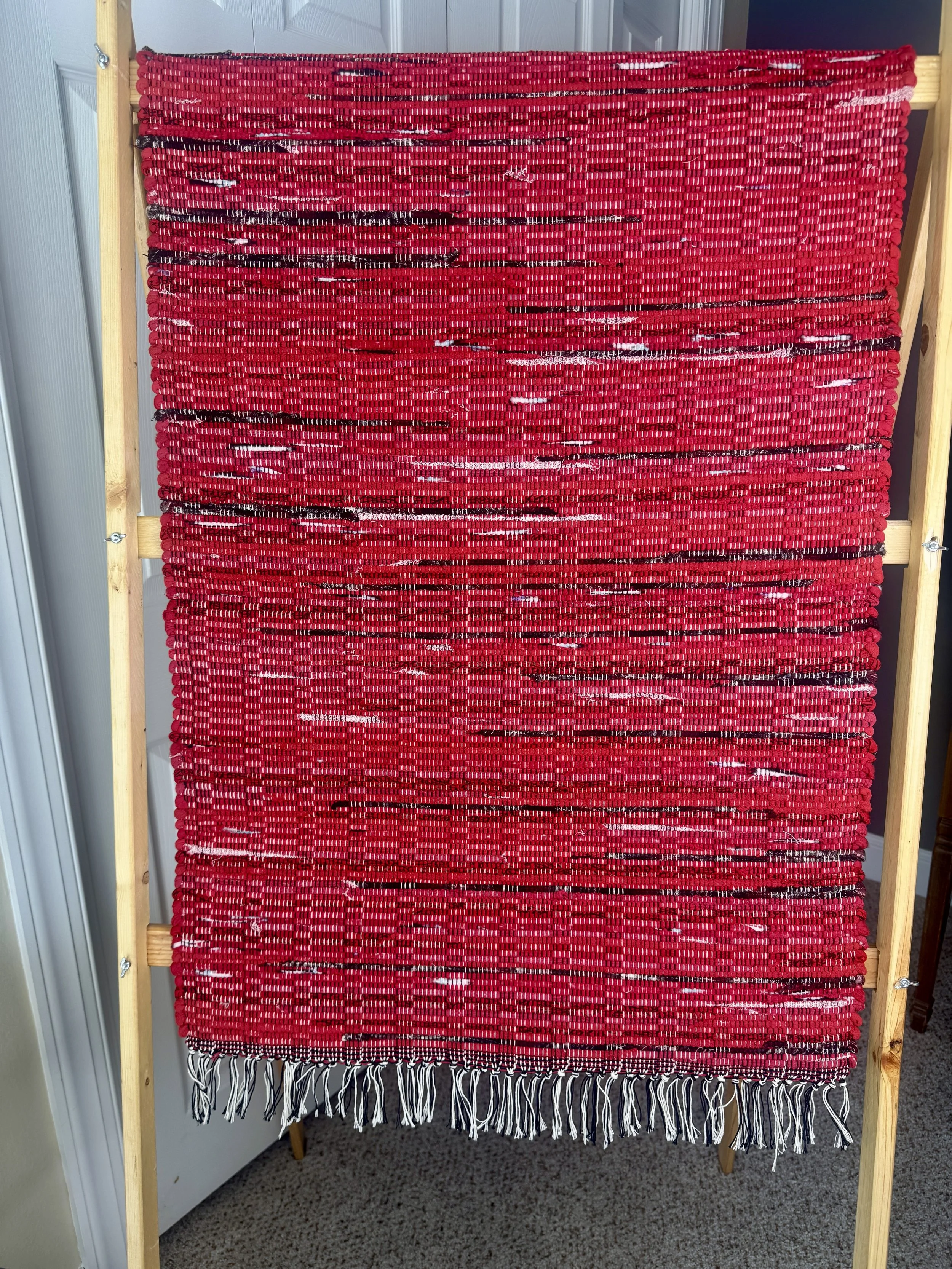 Hanging woven rag rug showing pattern and fringe