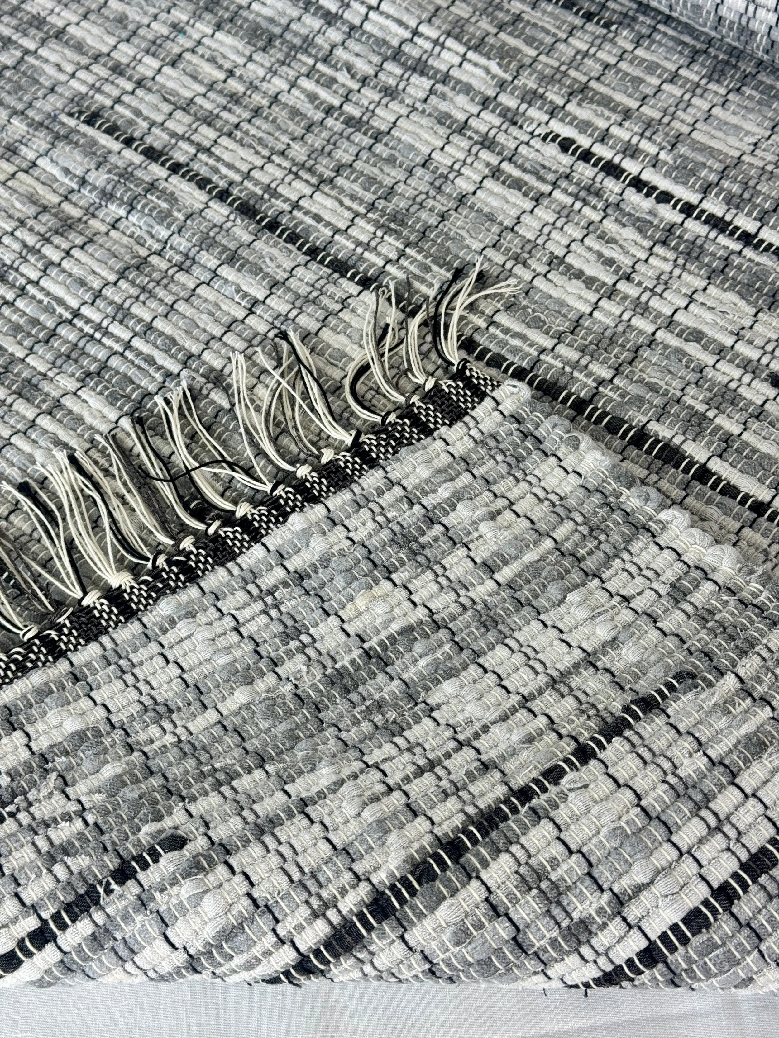 Folded handwoven rag rug showing reverse side and fringe