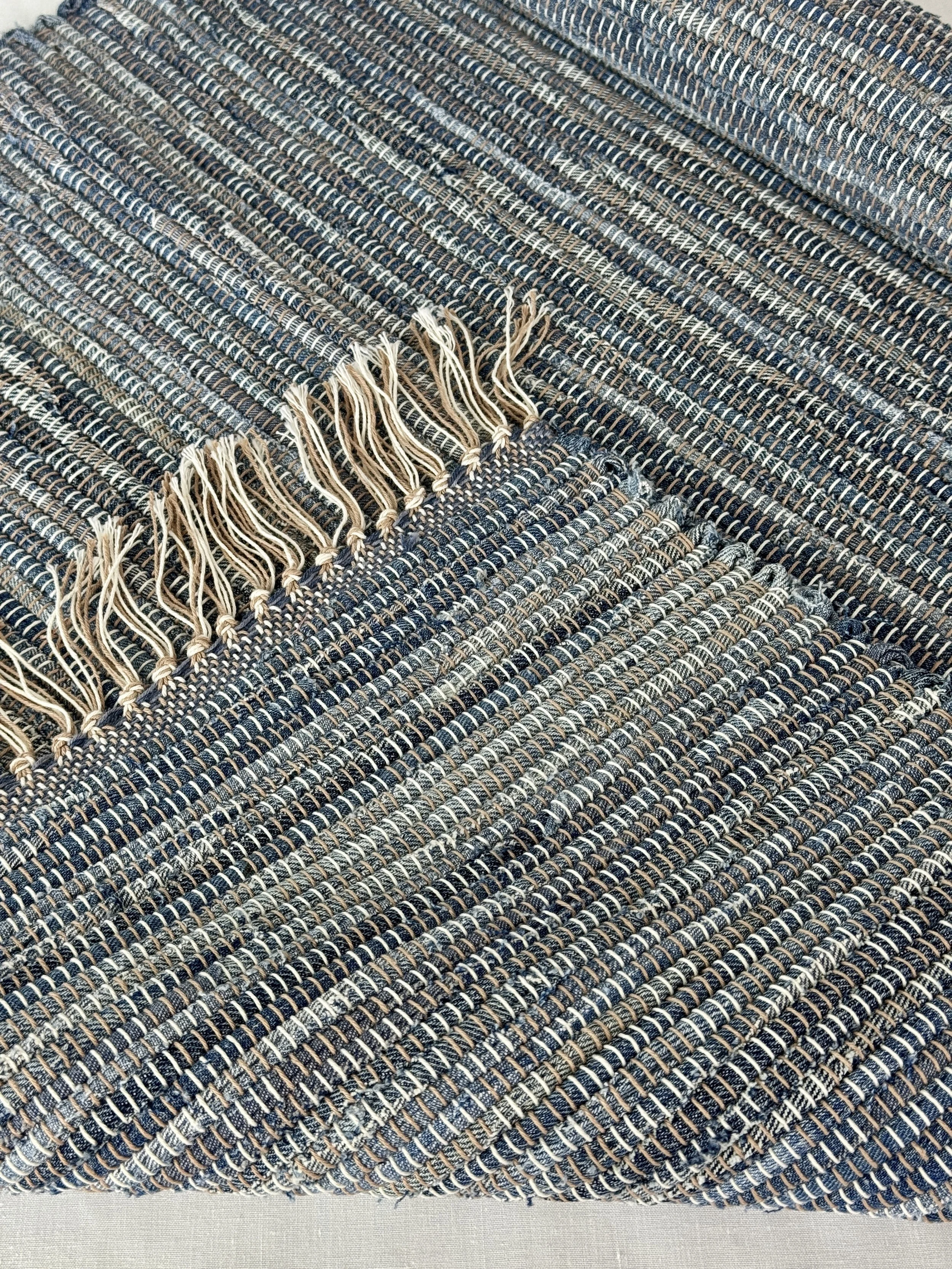 Folded handwoven recycled denim rag rug showing texture and fringe