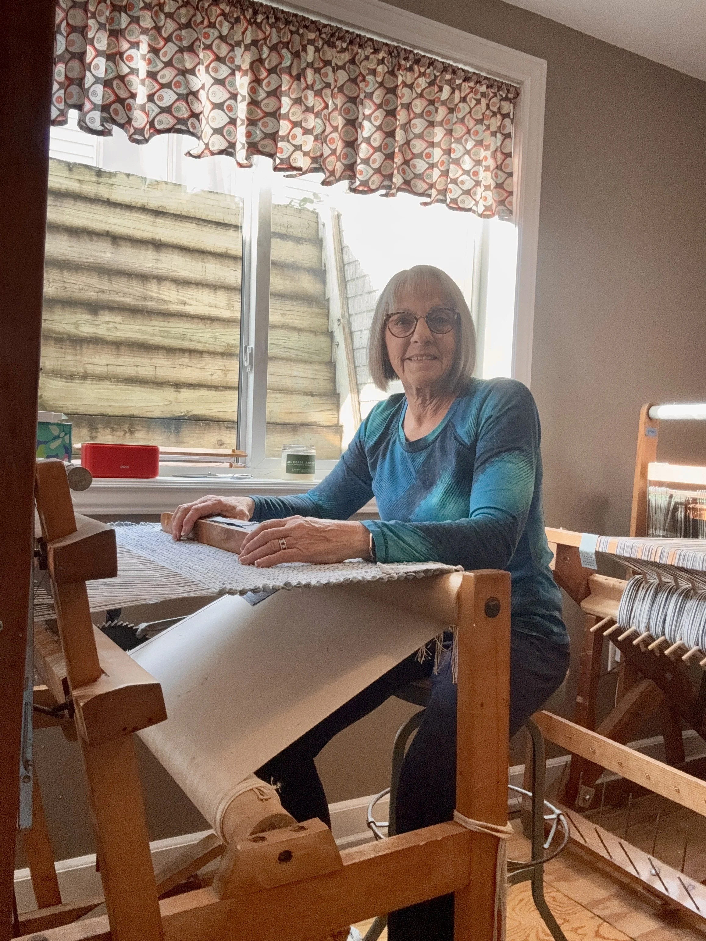 Terry weaving a handwoven rag rug on a wooden floor loom in her home