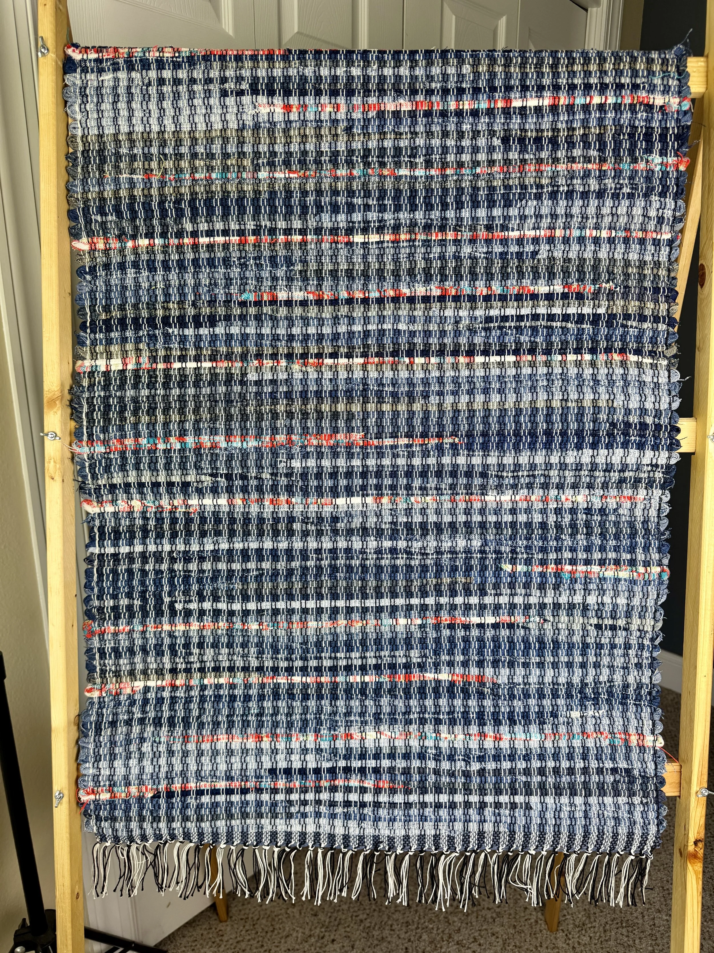 Hanging handmade upcycled blue jeans rag rug showing pattern and fringe