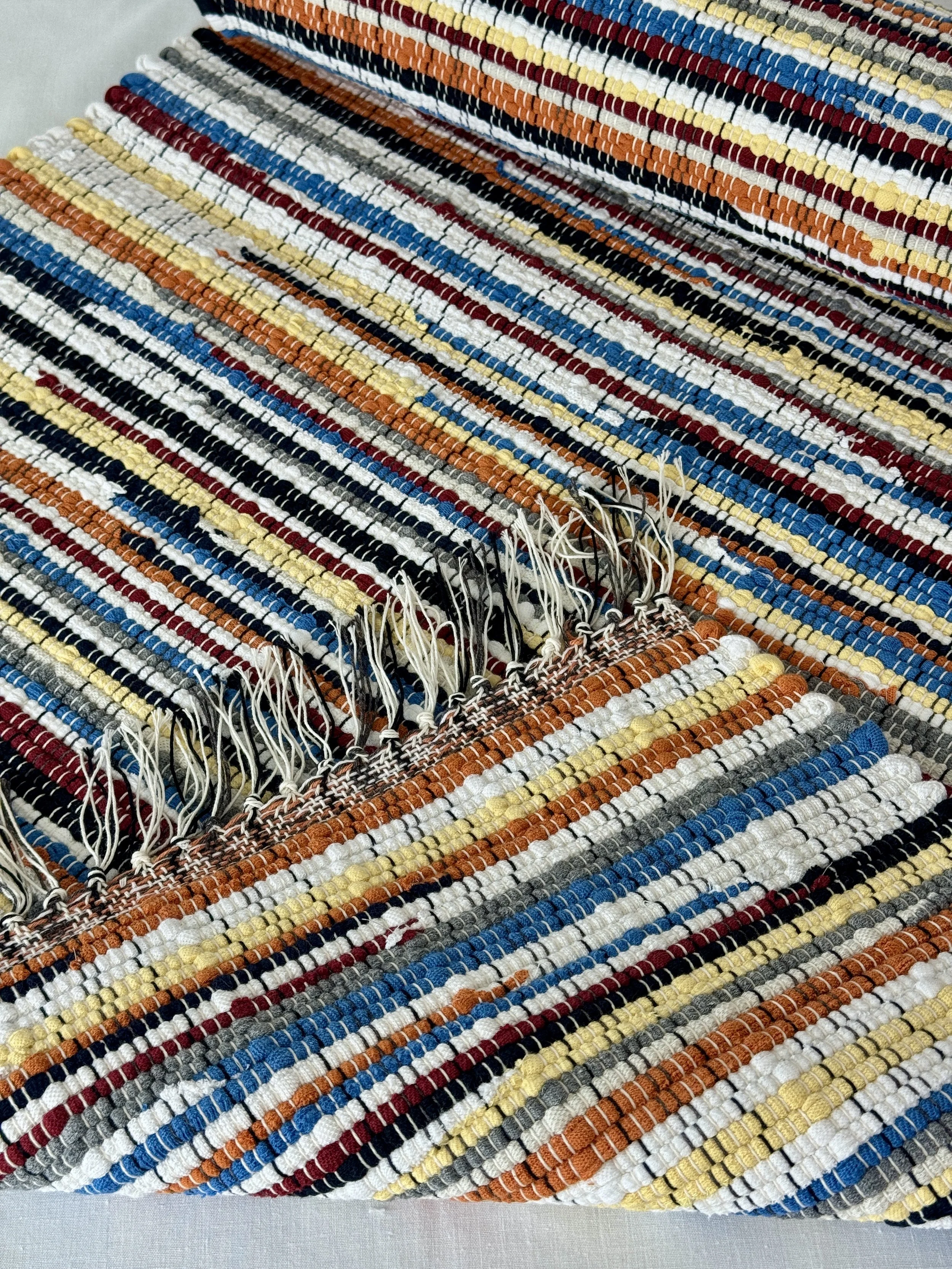 Folded handwoven rag rug showing reverse side and fringe