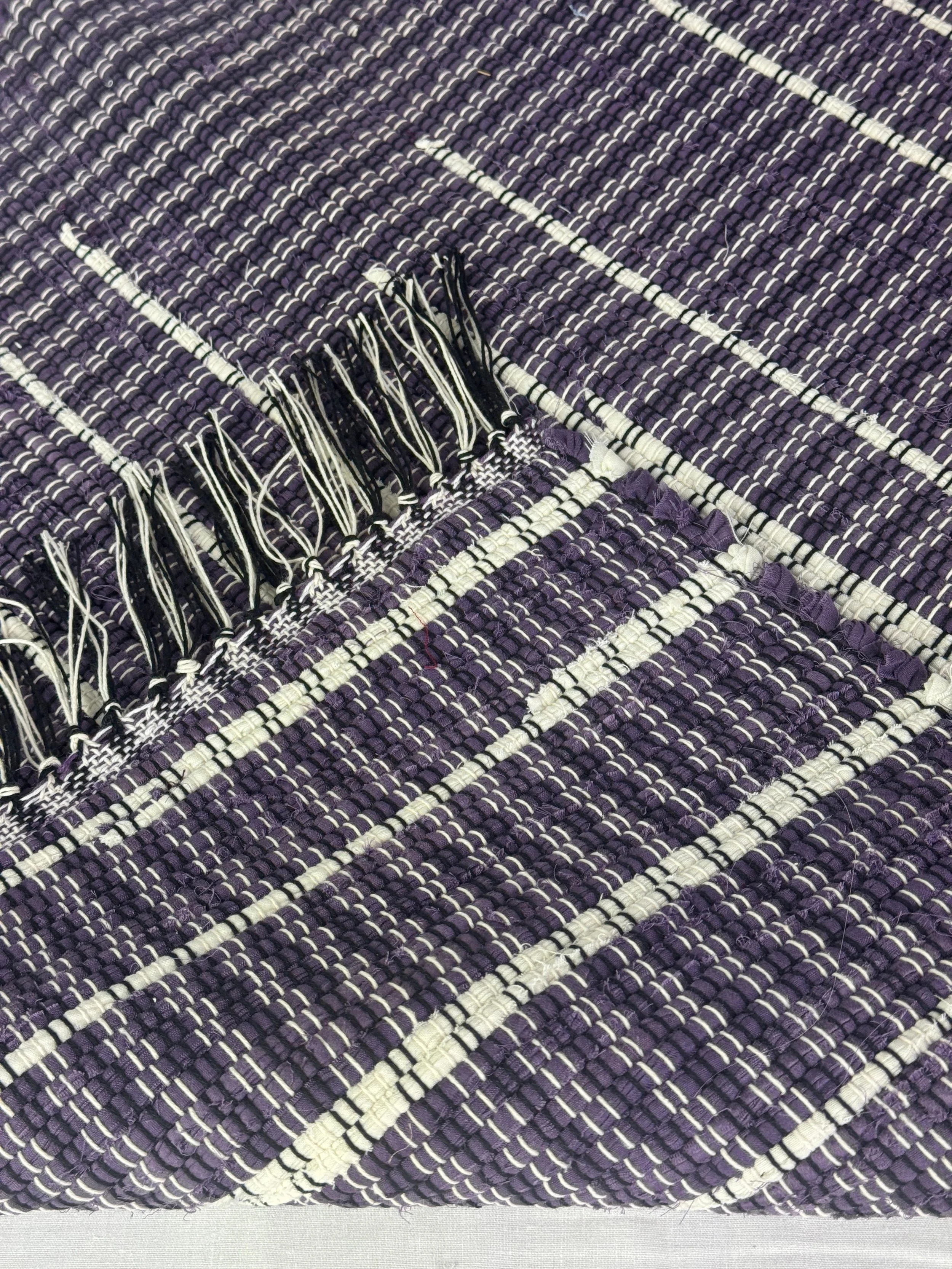 Handwoven purple/white folded rug showing reverse side and fringe