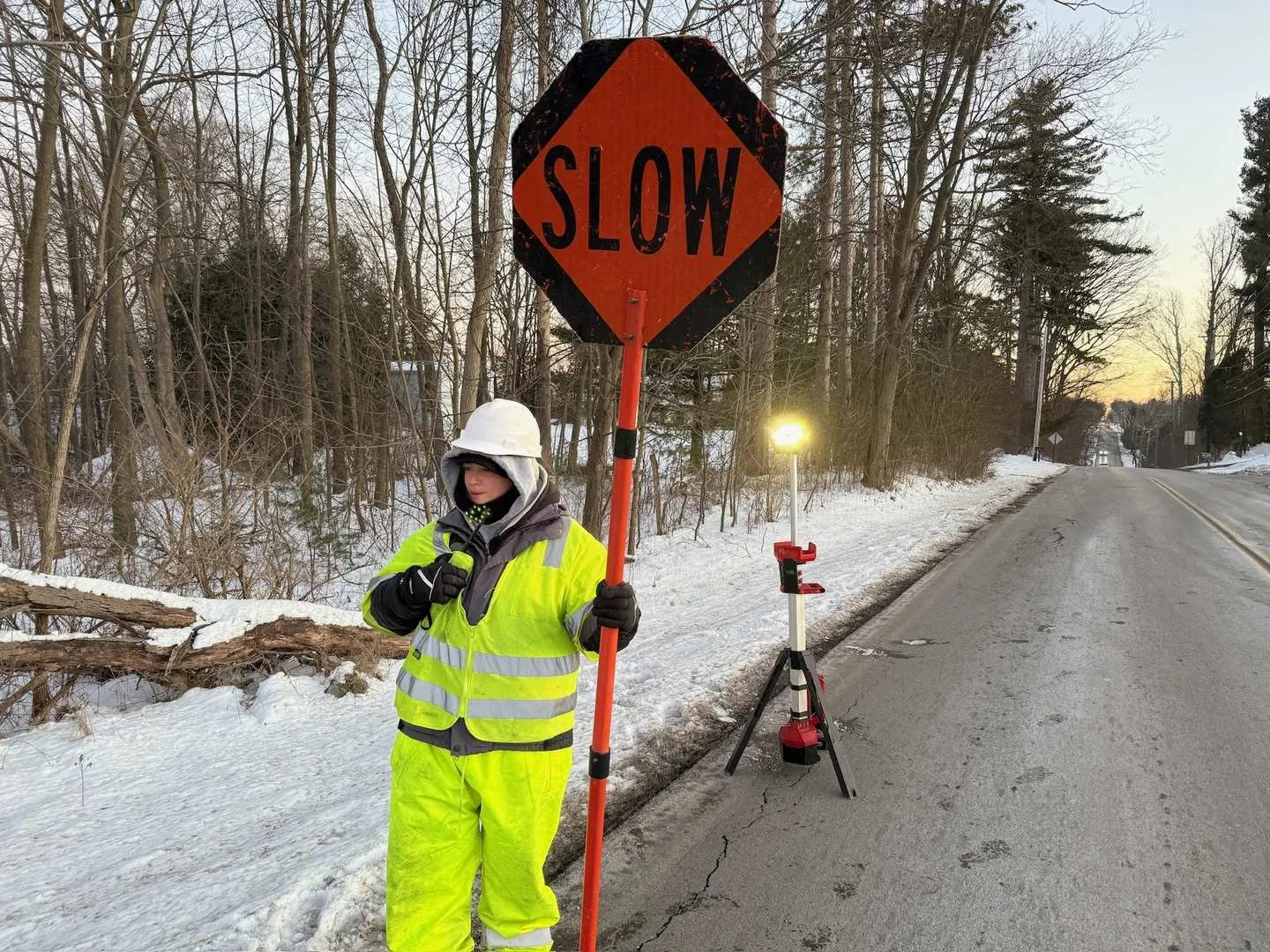 Construction flagger in high-visibility gear manages traffic on a winter road, ensuring safety in a work zone.