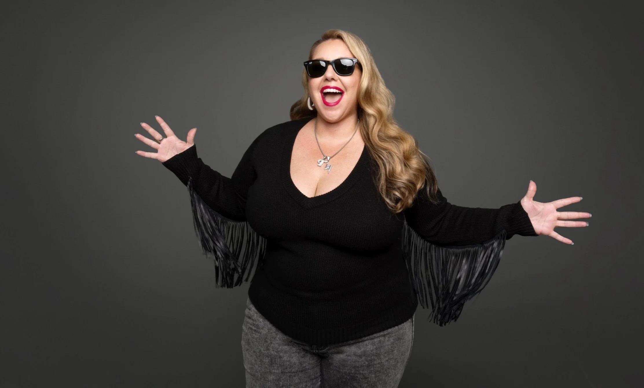 smiling woman with long blonde hair in sunglasses and black sweater with fringe