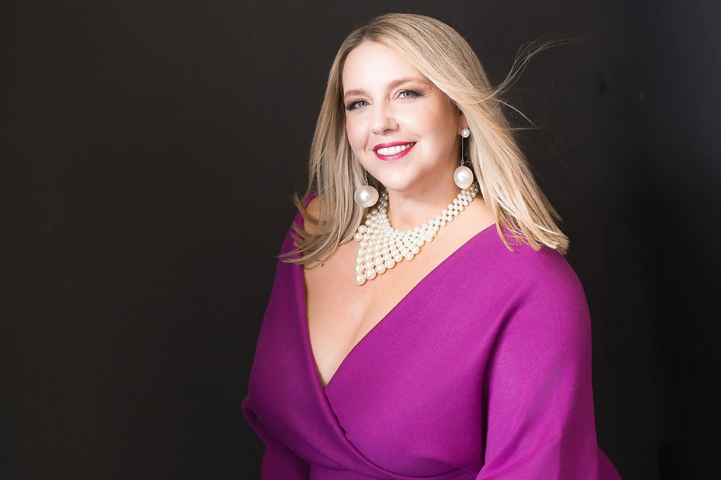 portrait of woman in purple dress with pearl necklace and earrings and dark background