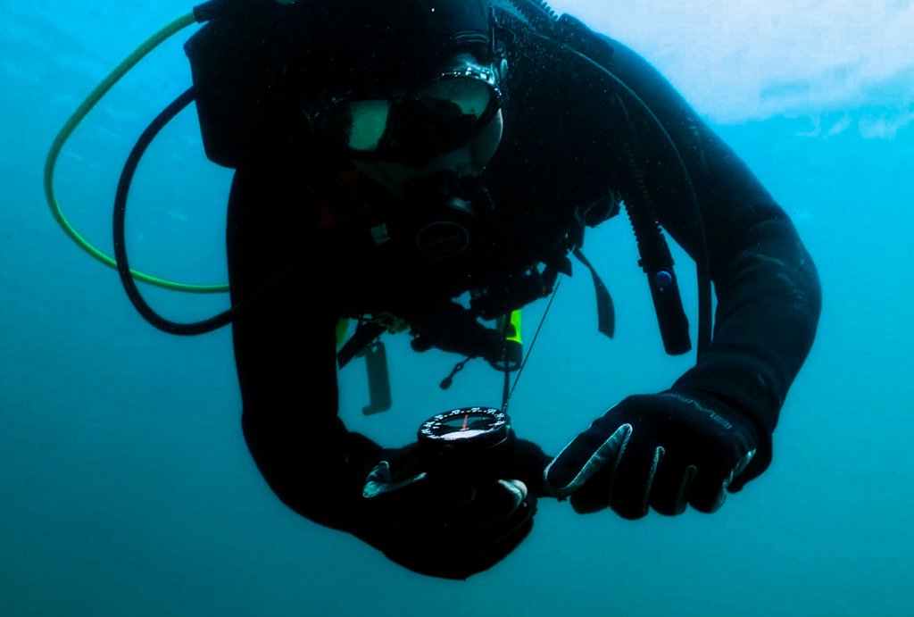 scuba diver uses retractable gear keeper clip accessory to read compass underwater