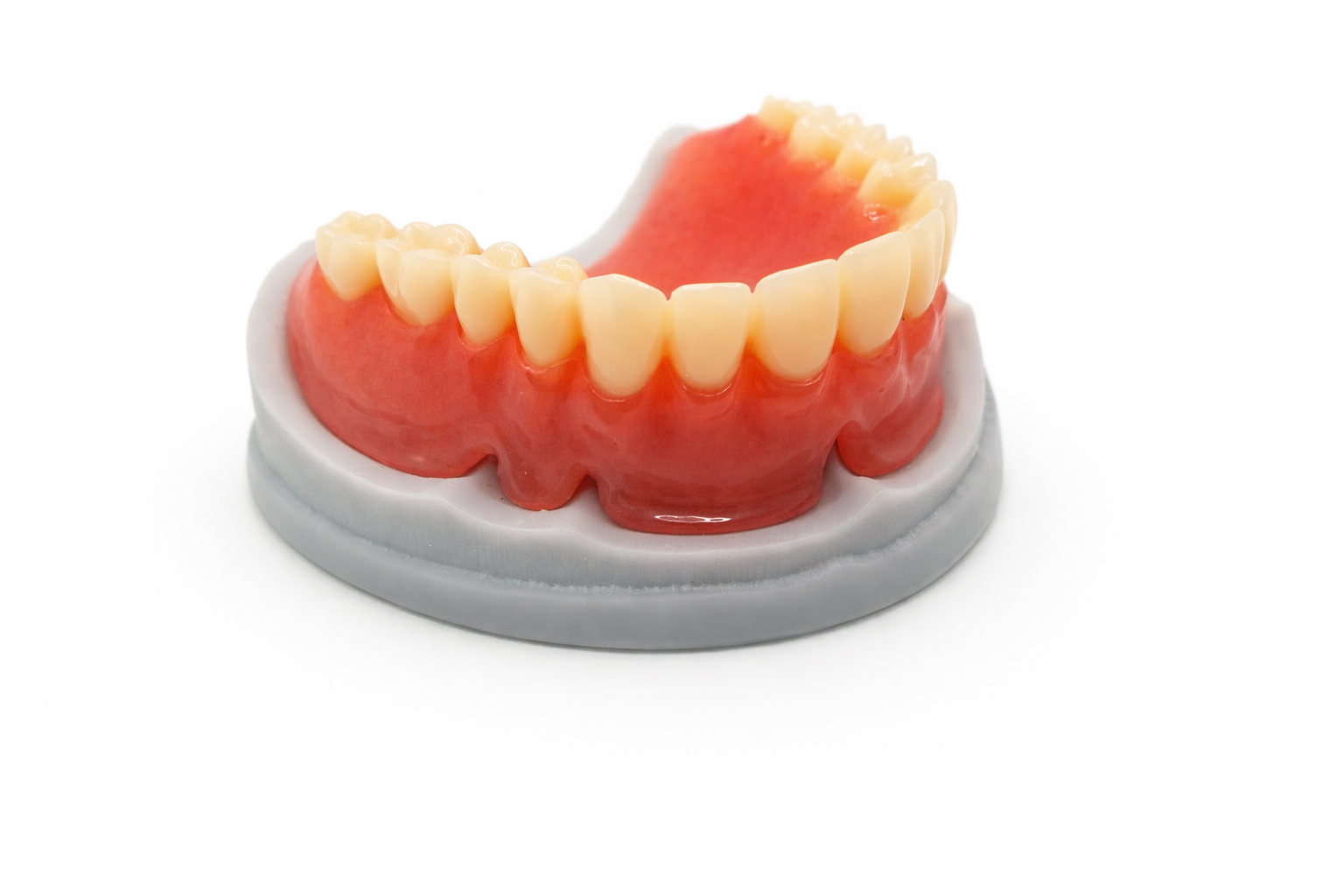 A set of false upper teeth dentures on a white base, with a pink gum section, isolated on a white background.