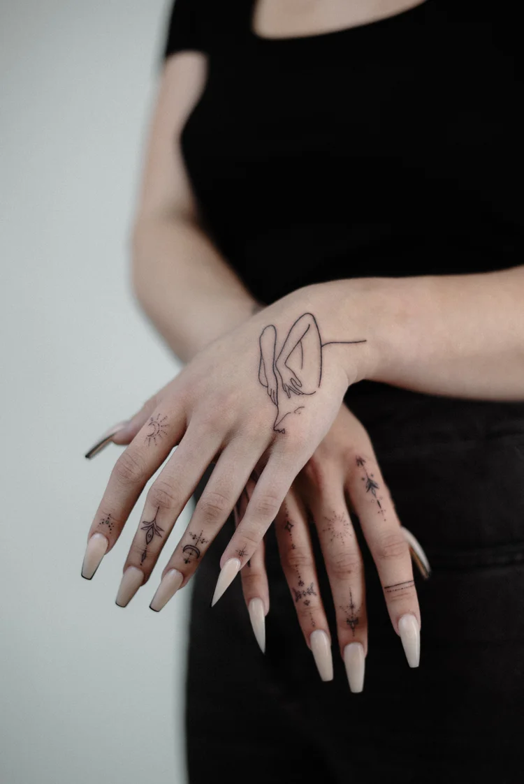 Fine line hand tattoos with line-art figure and small finger symbols