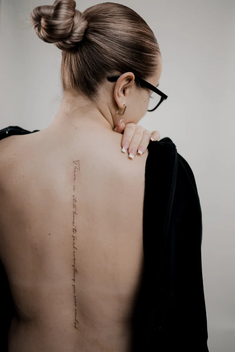 Delicate script tattoo running down the spine