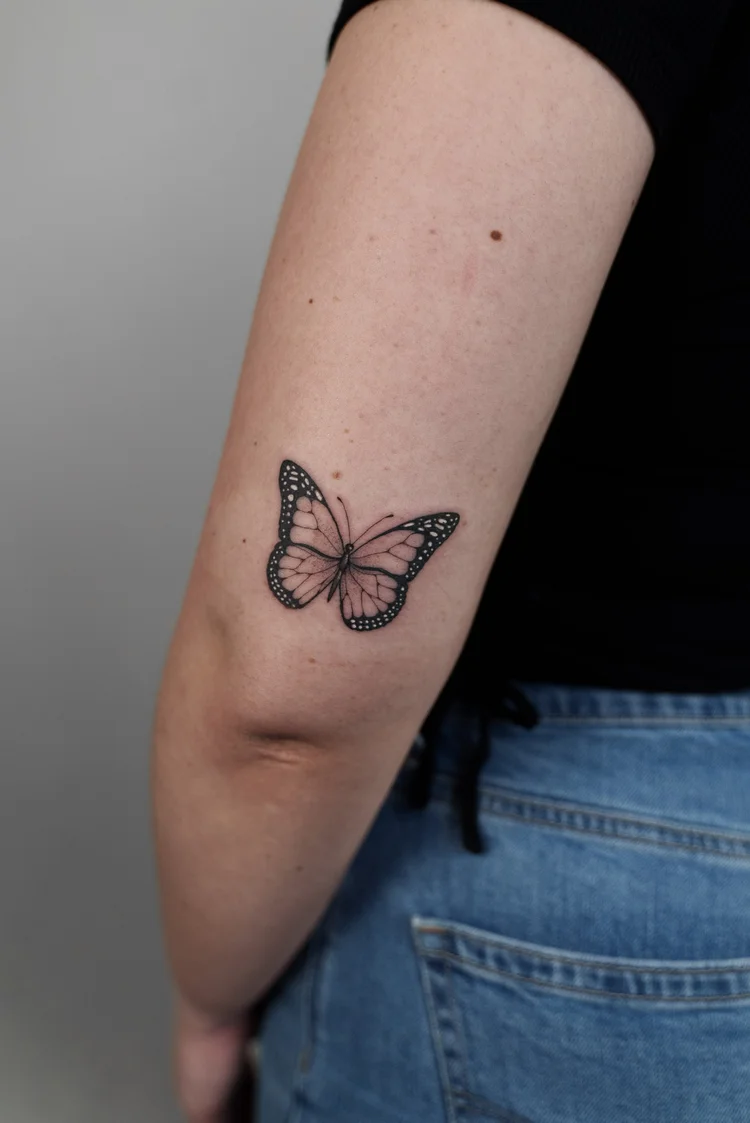 Black and grey monarch butterfly tattoo on the back of the arm