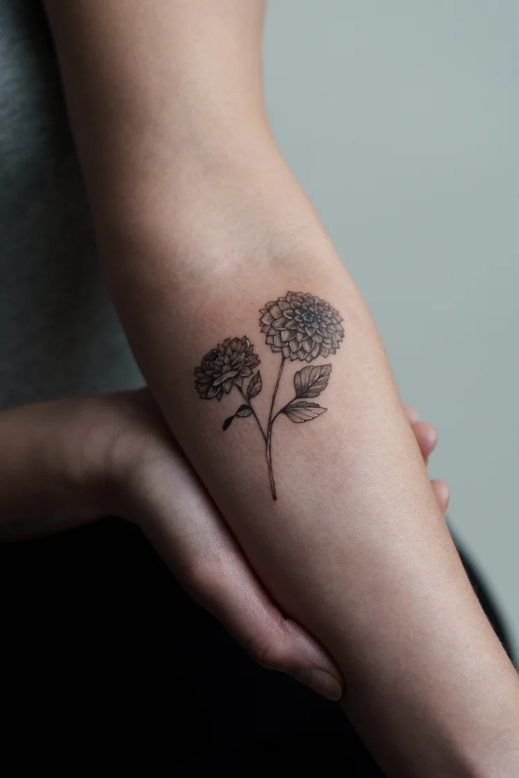 Fine line floral tattoo of two blooms on the inner forearm