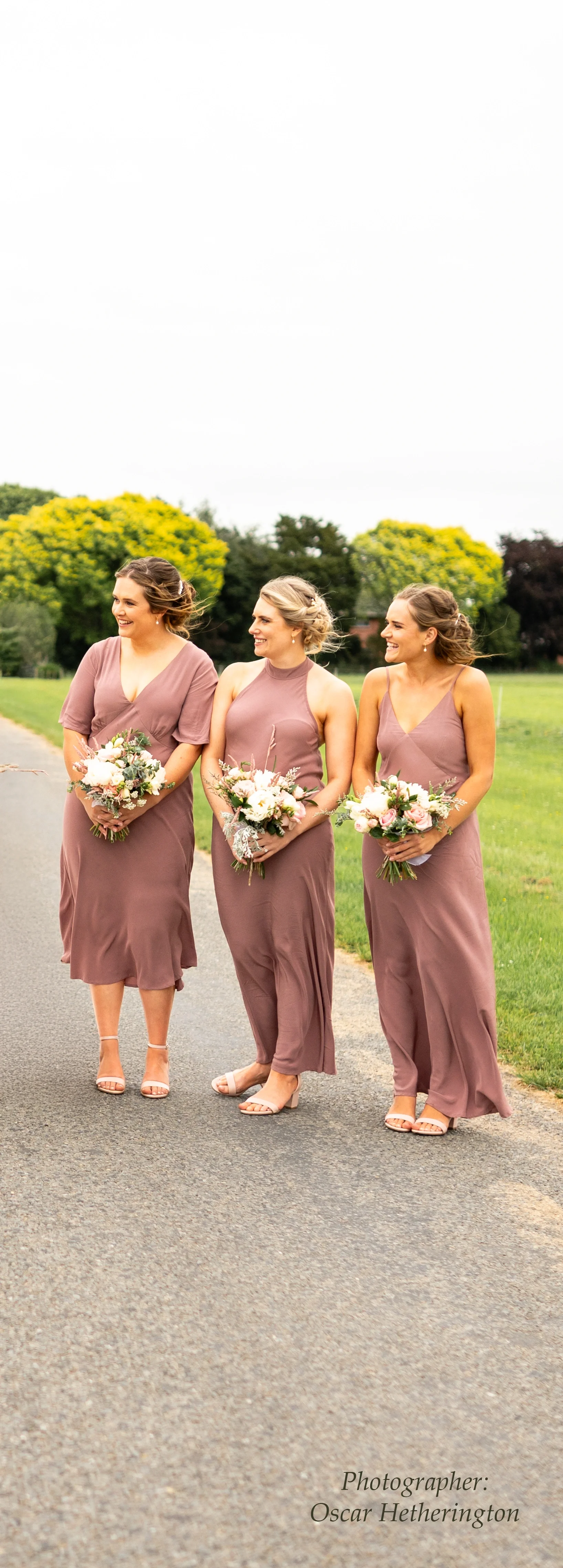 Three bridesmaids posing in beautifully fitted dusty rose floor-length gowns, each holding a white and green floral bouquet — expert bridal party dress alterations for a perfect fit
