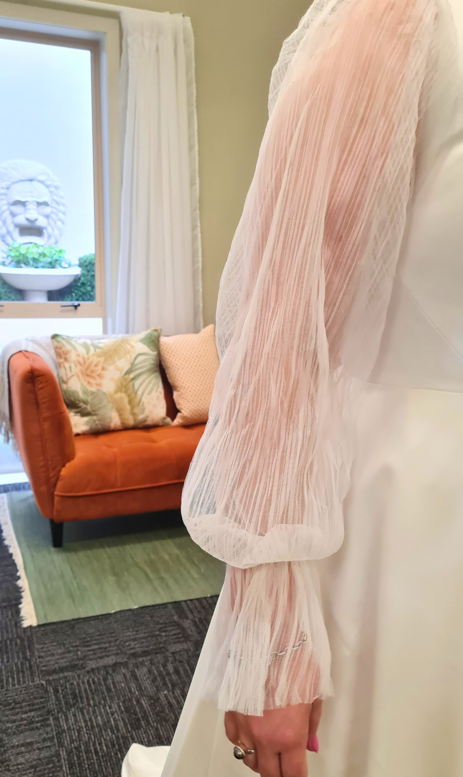 Bride wearing a ivory white wedding gown with sheer pleated tulle sleeves during a bridal fitting at Alena Hume's studio in Palmerston North