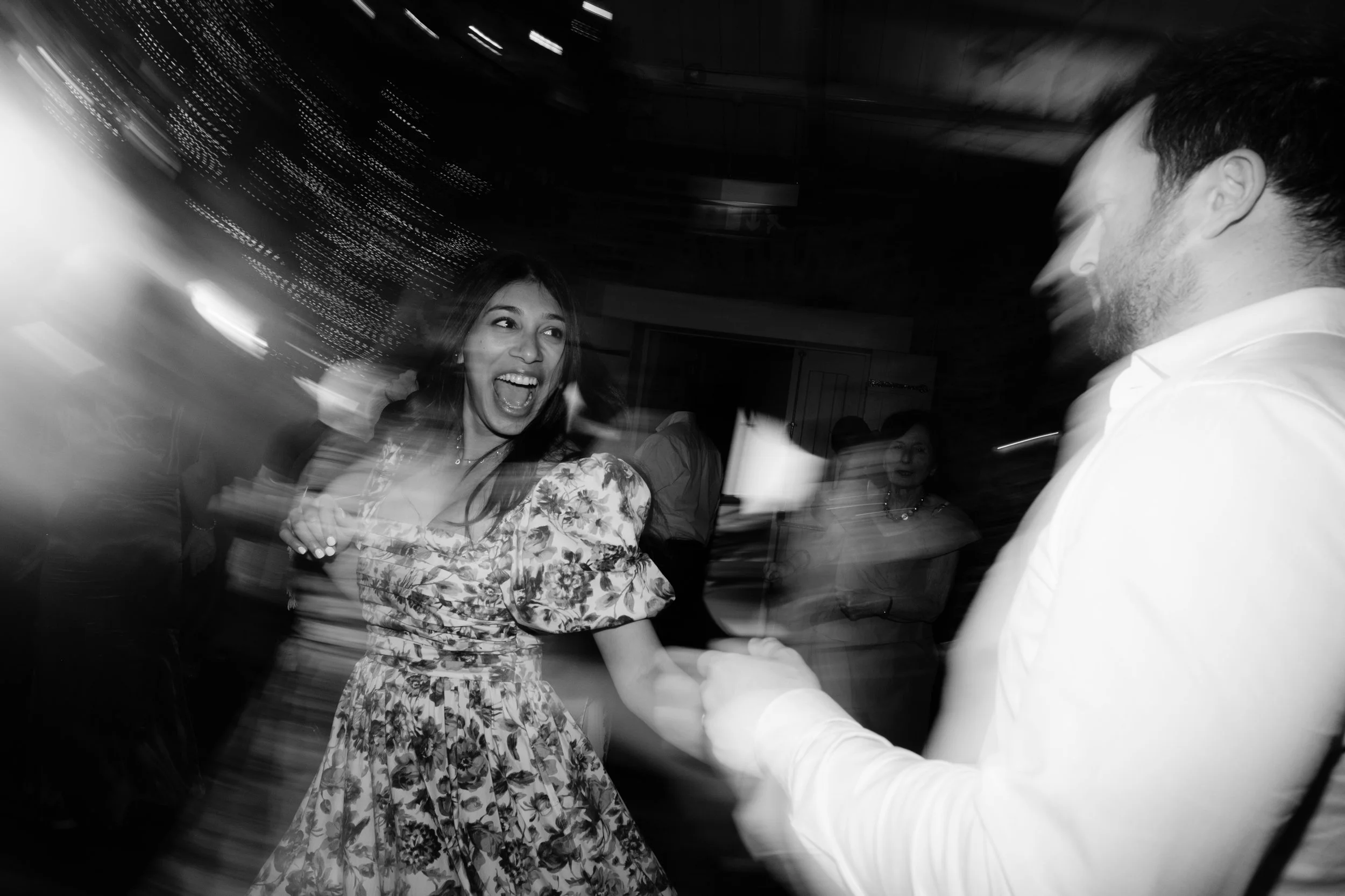 A woman in a floral dress and a man in a white shirt dancing and smiling at a party with blurred motion and lively atmosphere.