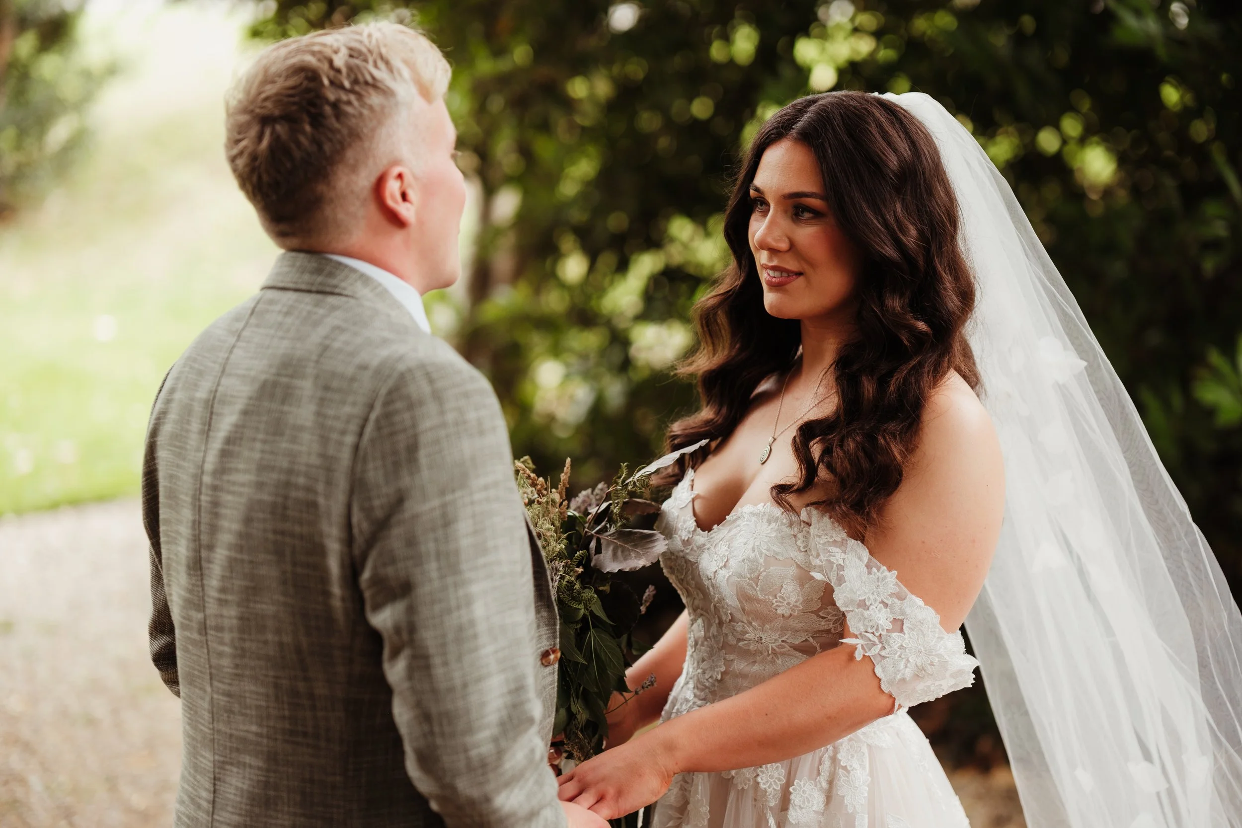 Bride and groom standing outdoors, holding hands and gazing at each other on their wedding day.