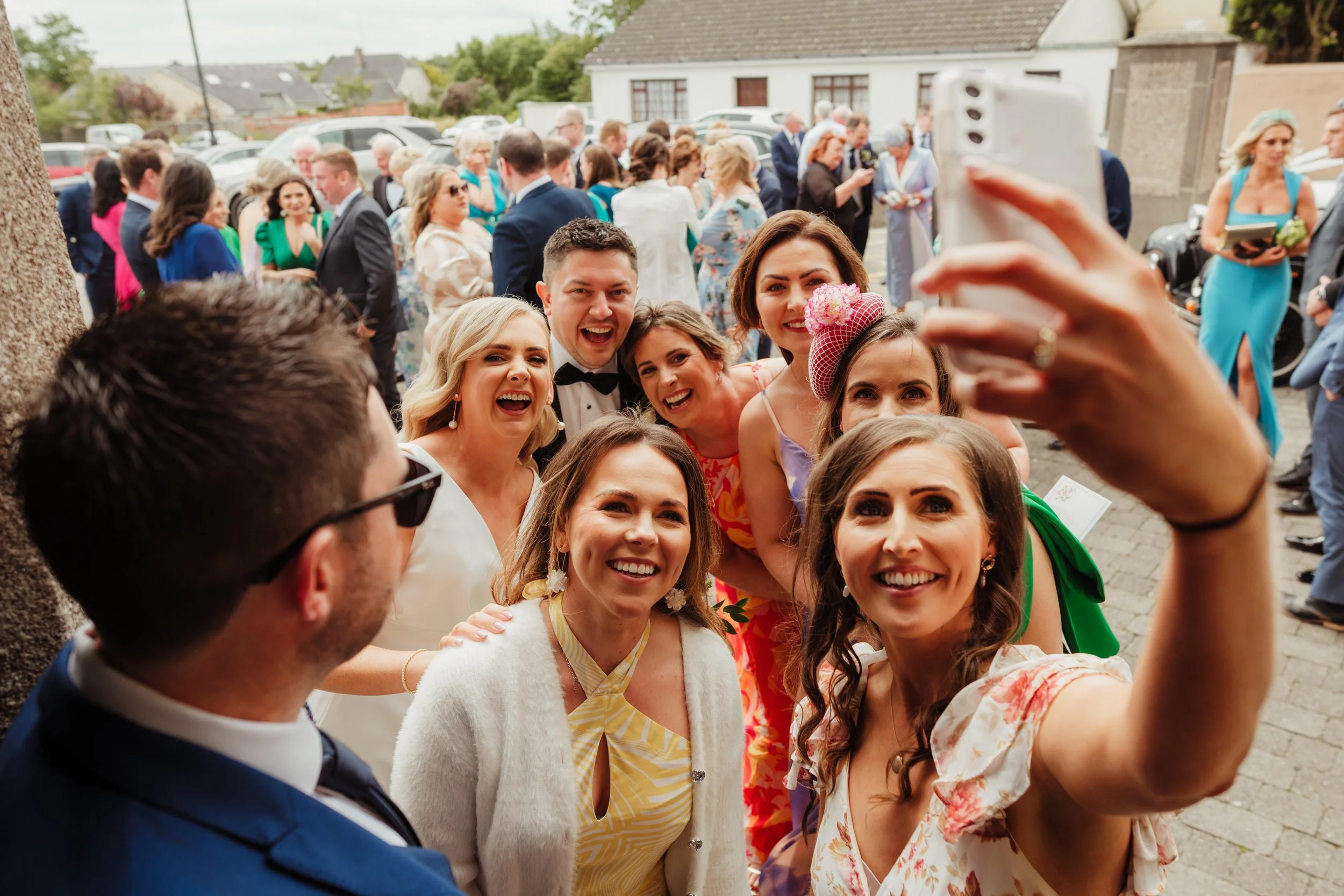 Group of friends dressed in formal attire taking a selfie outdoors at a wedding celebration