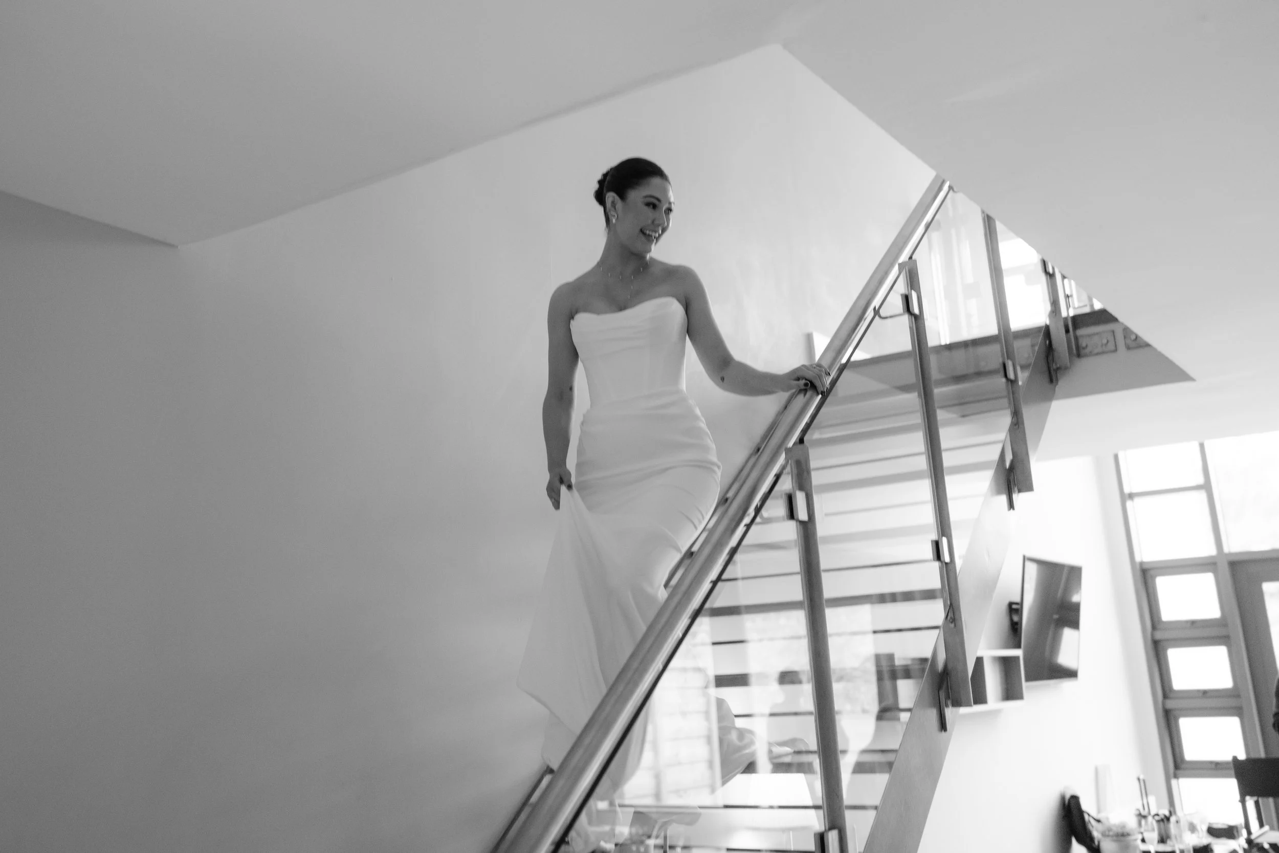 A woman in a strapless white dress ascending a staircase inside a modern building.