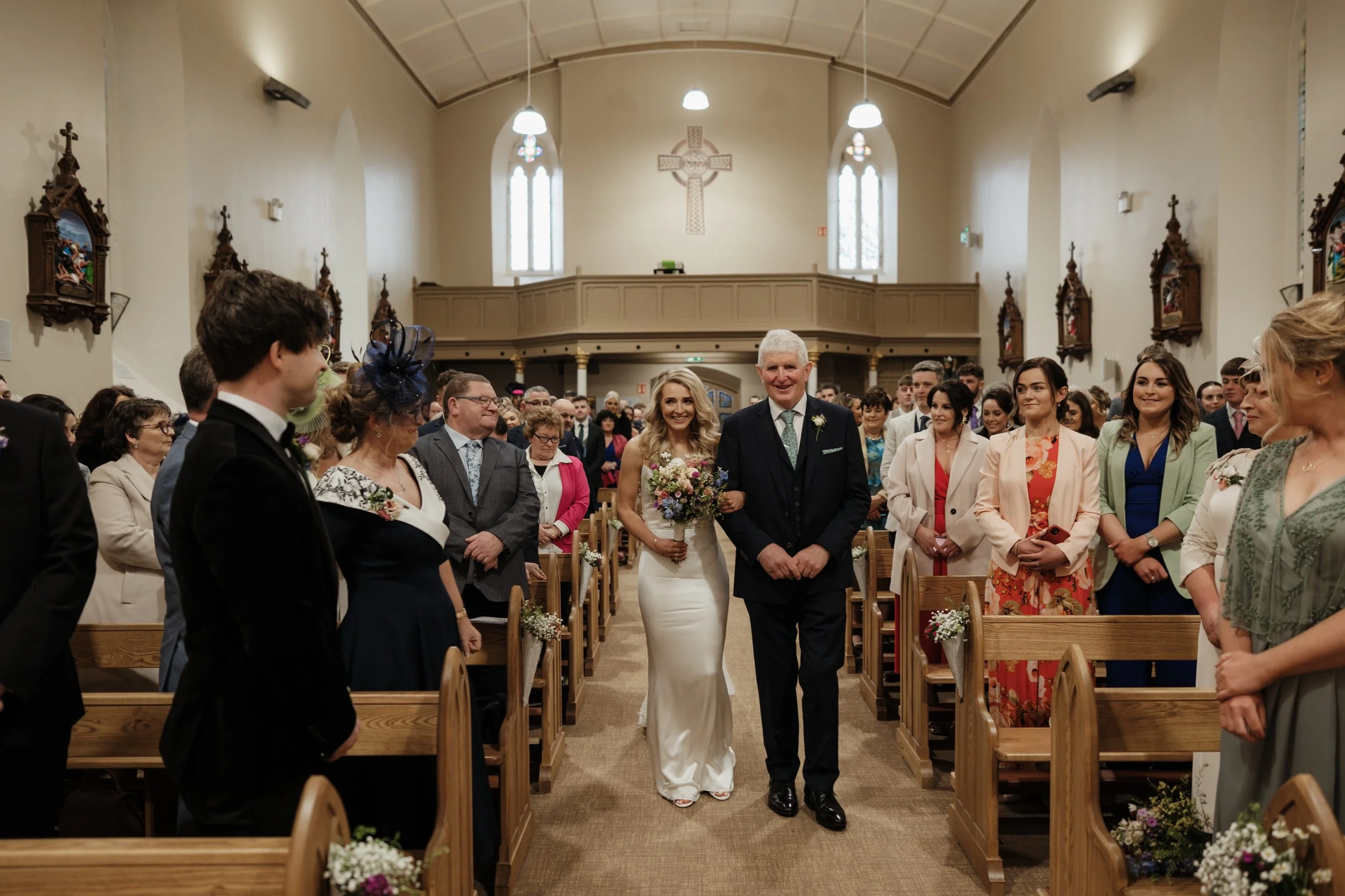 Bride walking down the aisle with her father in a church filled with guests, during a wedding ceremony.